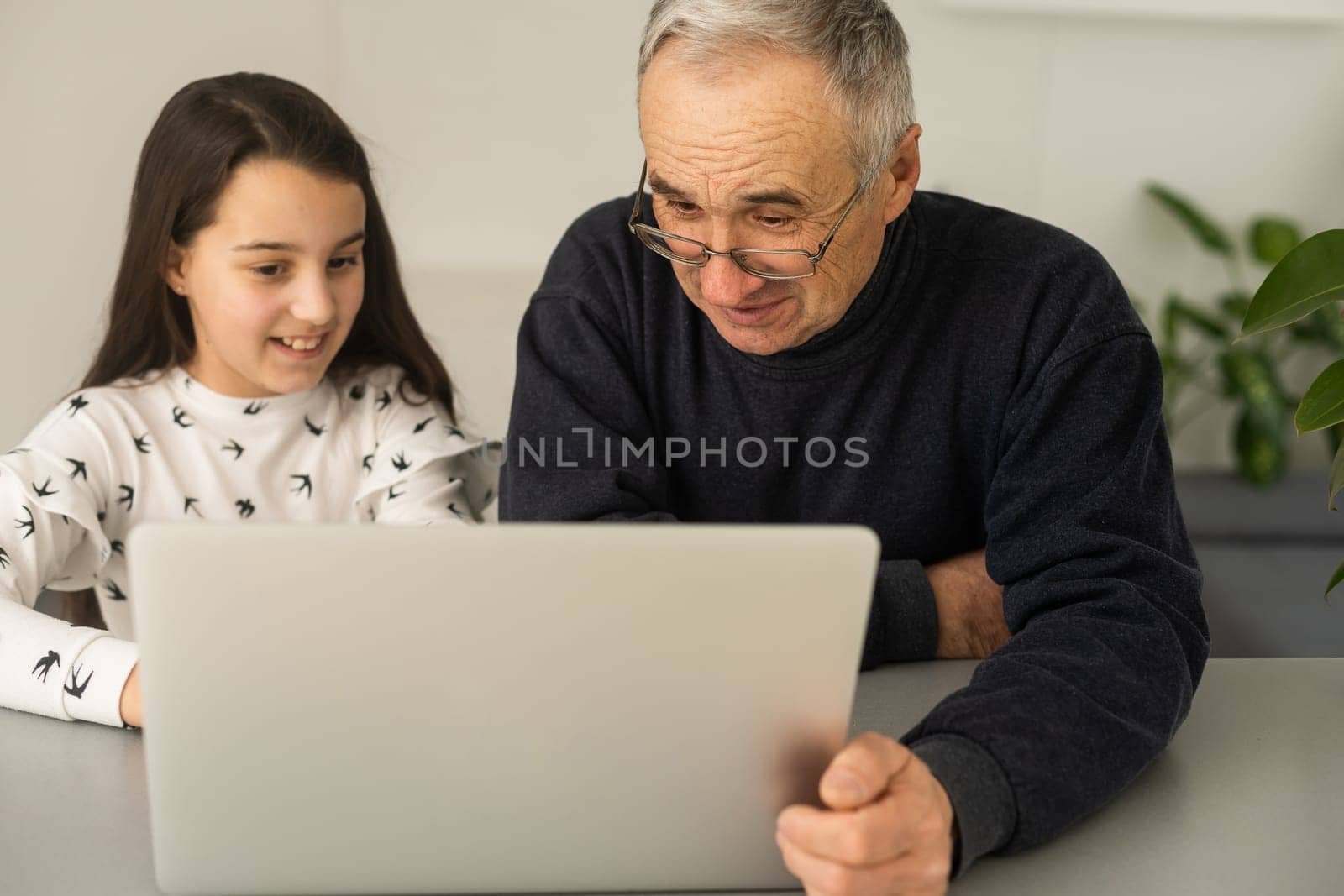 Portrait of senior man and young girl granddaughter using laptop at home