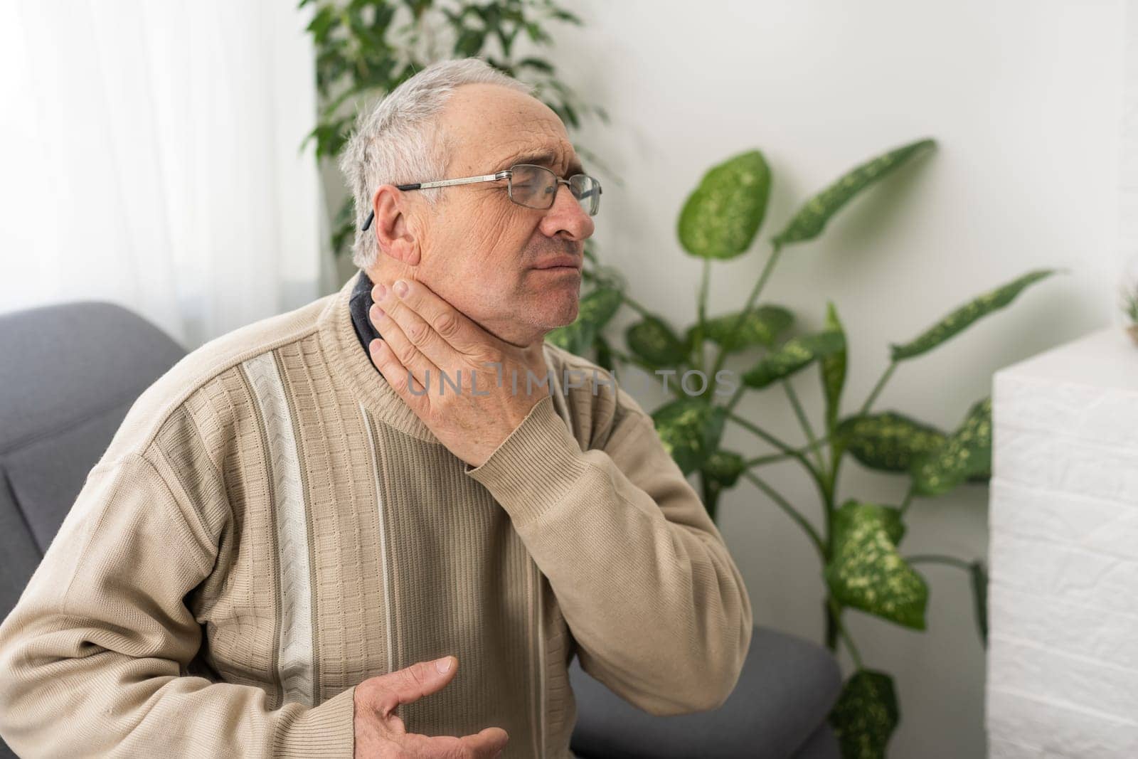Elderly Man Having Toothache Touching Cheek Suffering From Pain Sitting On Sofa At Home. by Andelov13