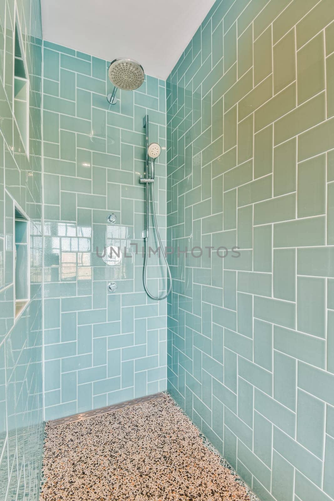 a bathroom with blue and white tiles on the walls, shower head in the corner to the floor is made out of pebbles