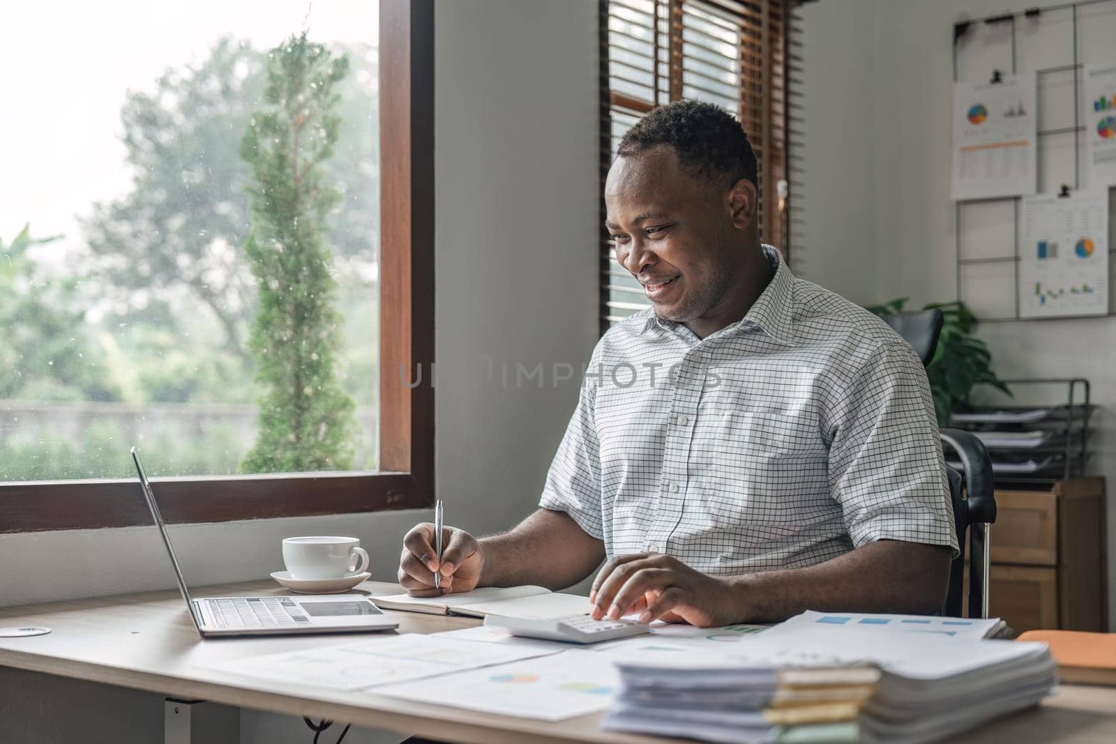 Happy black man planning budget, calculating expenses and taking notes in planner at home.