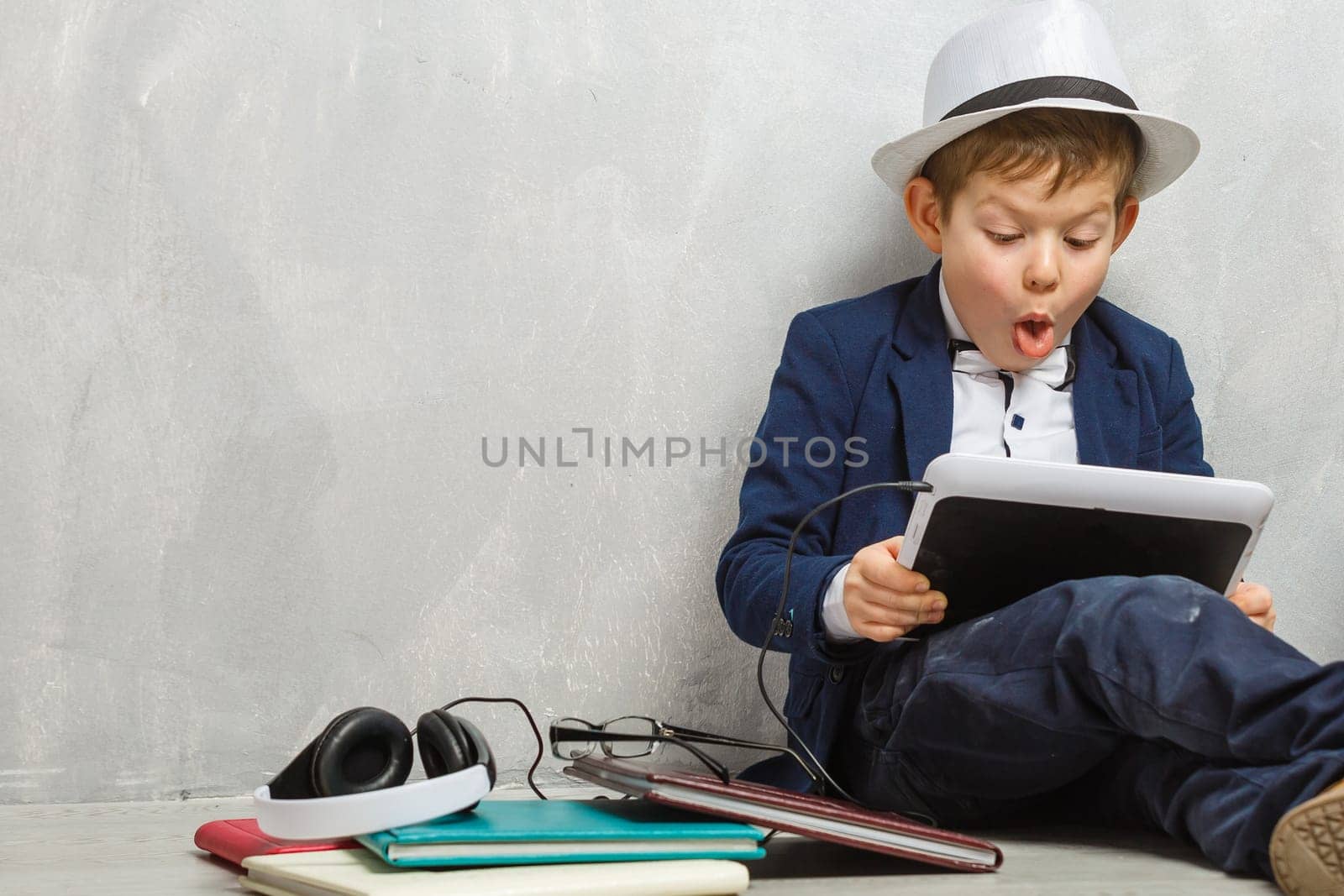 Cheerful little boy holding digital tablet against gray background. School concept. Back to School.