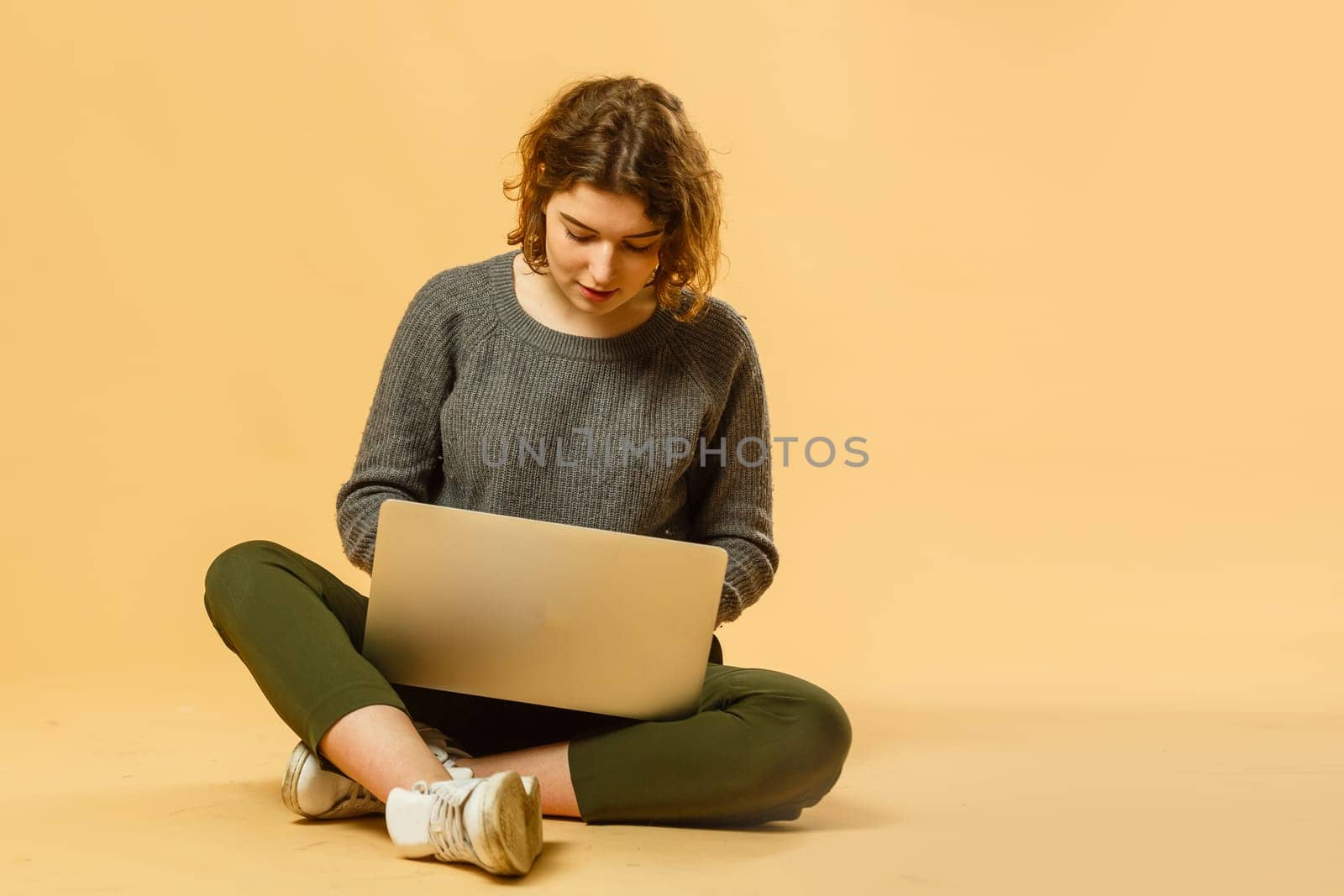 Smiling cheerful funny beautiful attractive young brunette woman 20s wearing basic casual working on laptop pc computer isolated on bright beige colour background studio portrait.