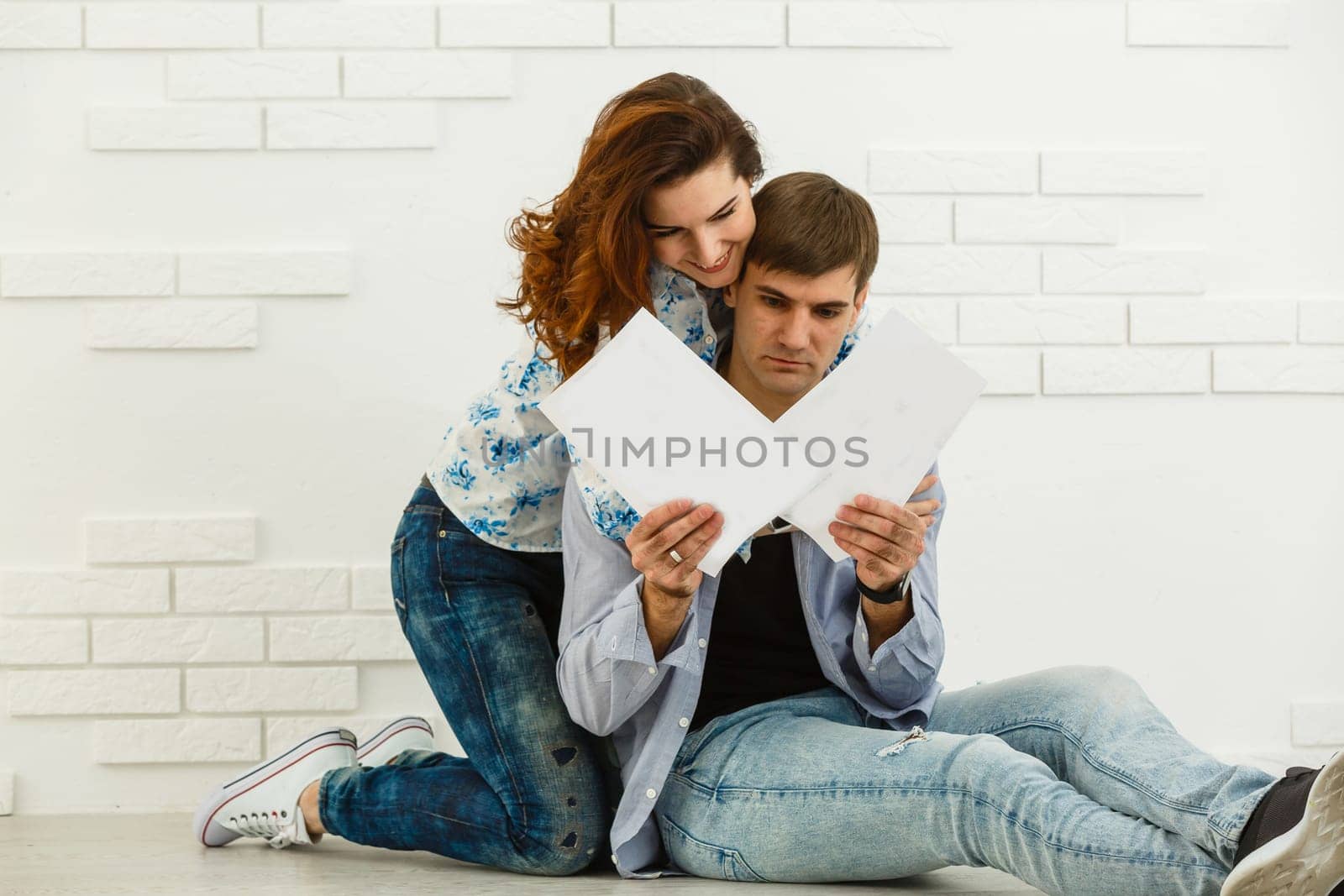 Smiling husband and wife sit taking care of utility bills and house maintenance documents, happy young couple read paperwork.