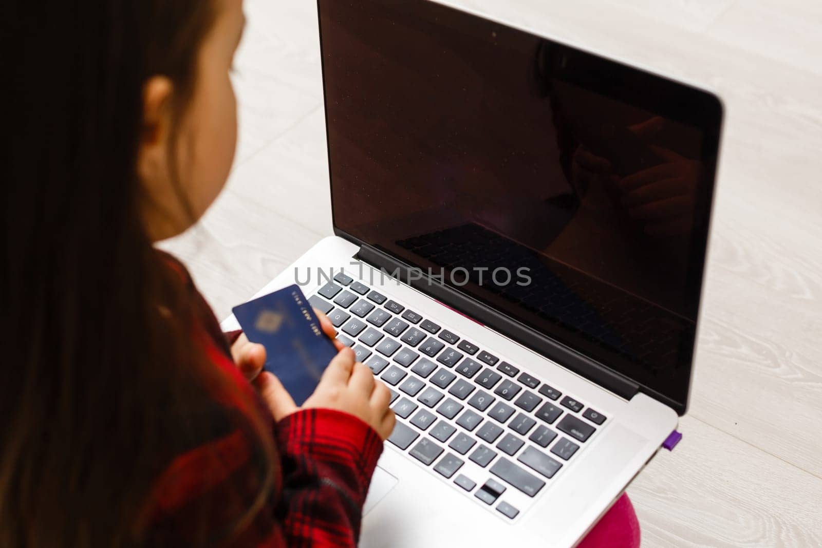 Happy little girl holding credit card buying online at home