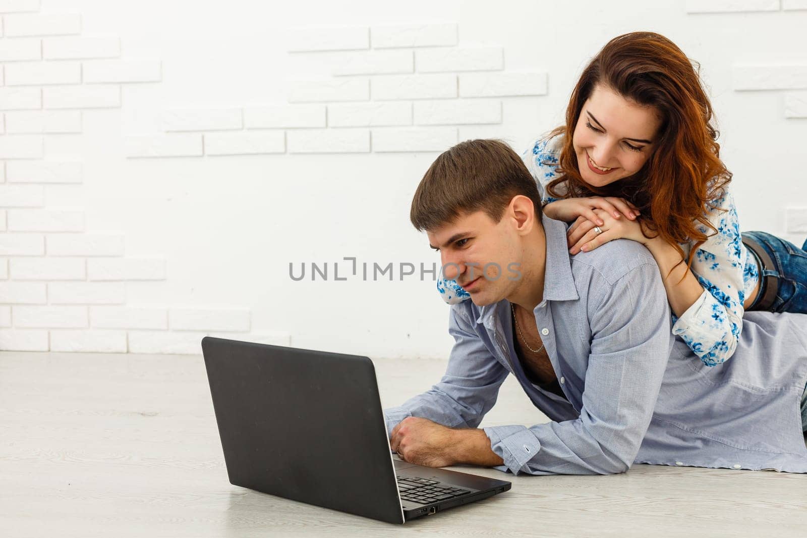 Couple Use Laptop Computer, while Sitting on the Living Floor room of their Apartment. Boyfriend and Girlfriend Talk, Shop on Internet, Choose Product to Order Online, Watch Streaming Service. by Andelov13
