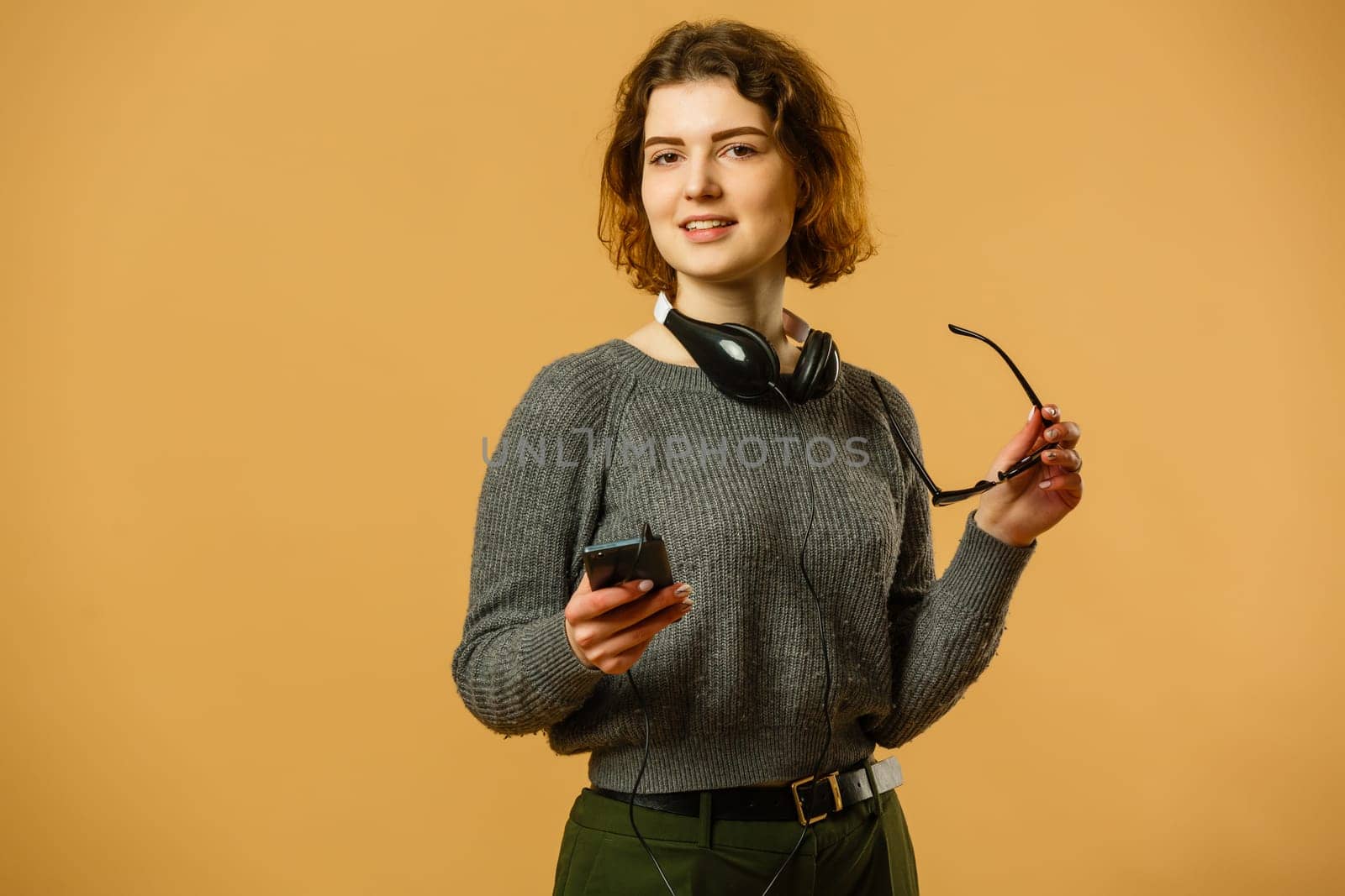 Smiling woman listening music in headphones and using smartphone over yellow background.