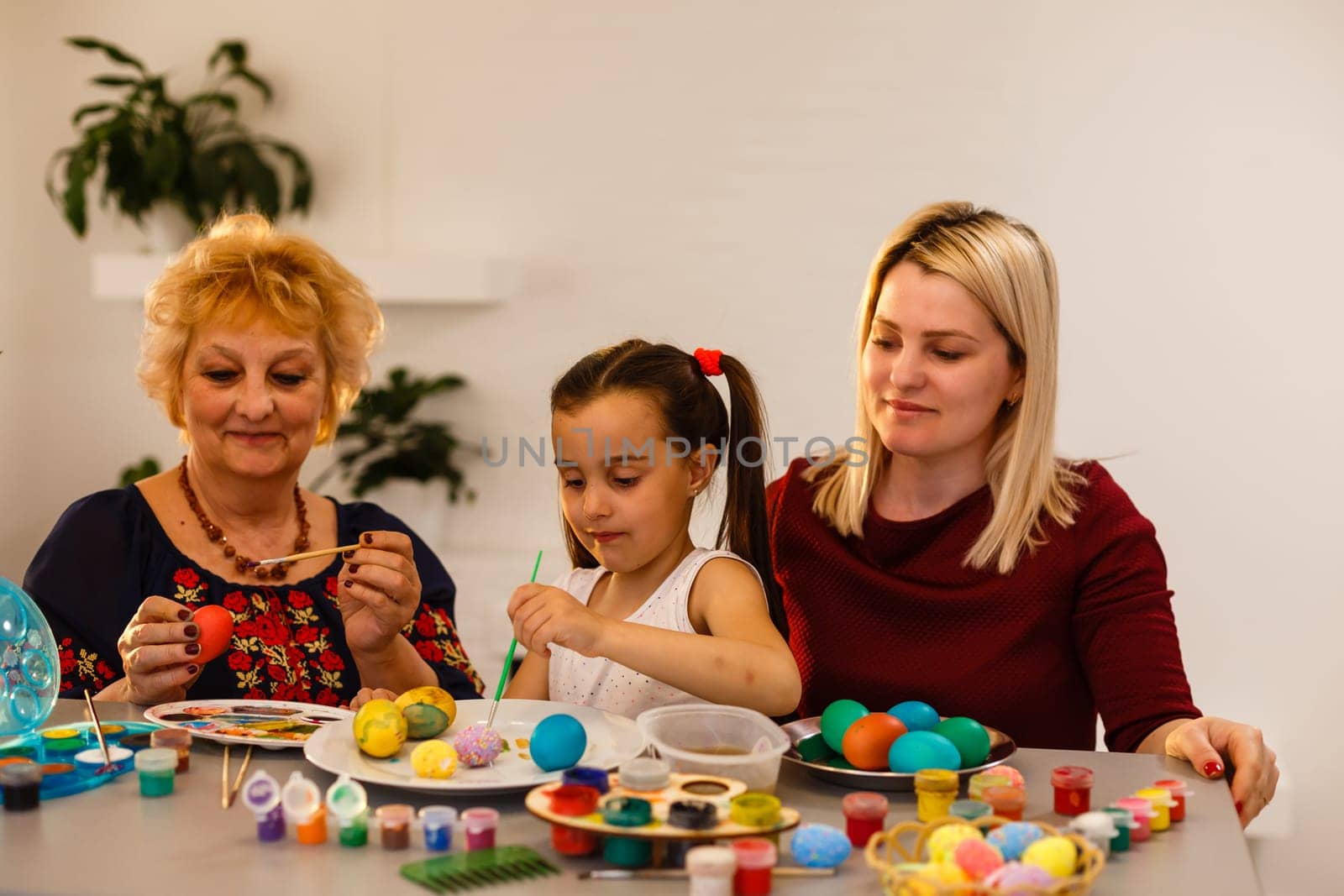 Little girl and her grandmother painting Easter eggs at home