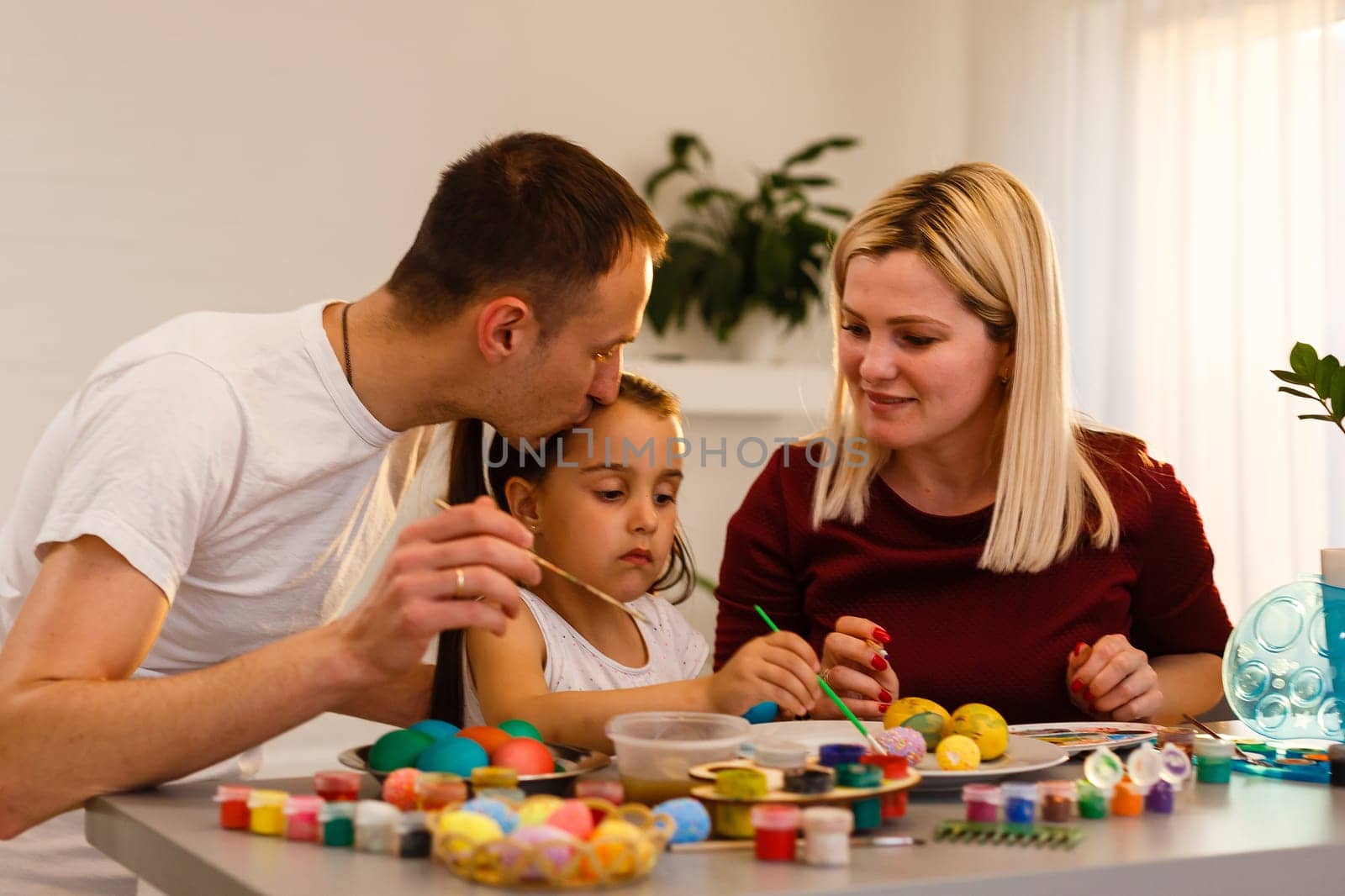 Happy family painting Easter eggs at table in kitchen. by Andelov13