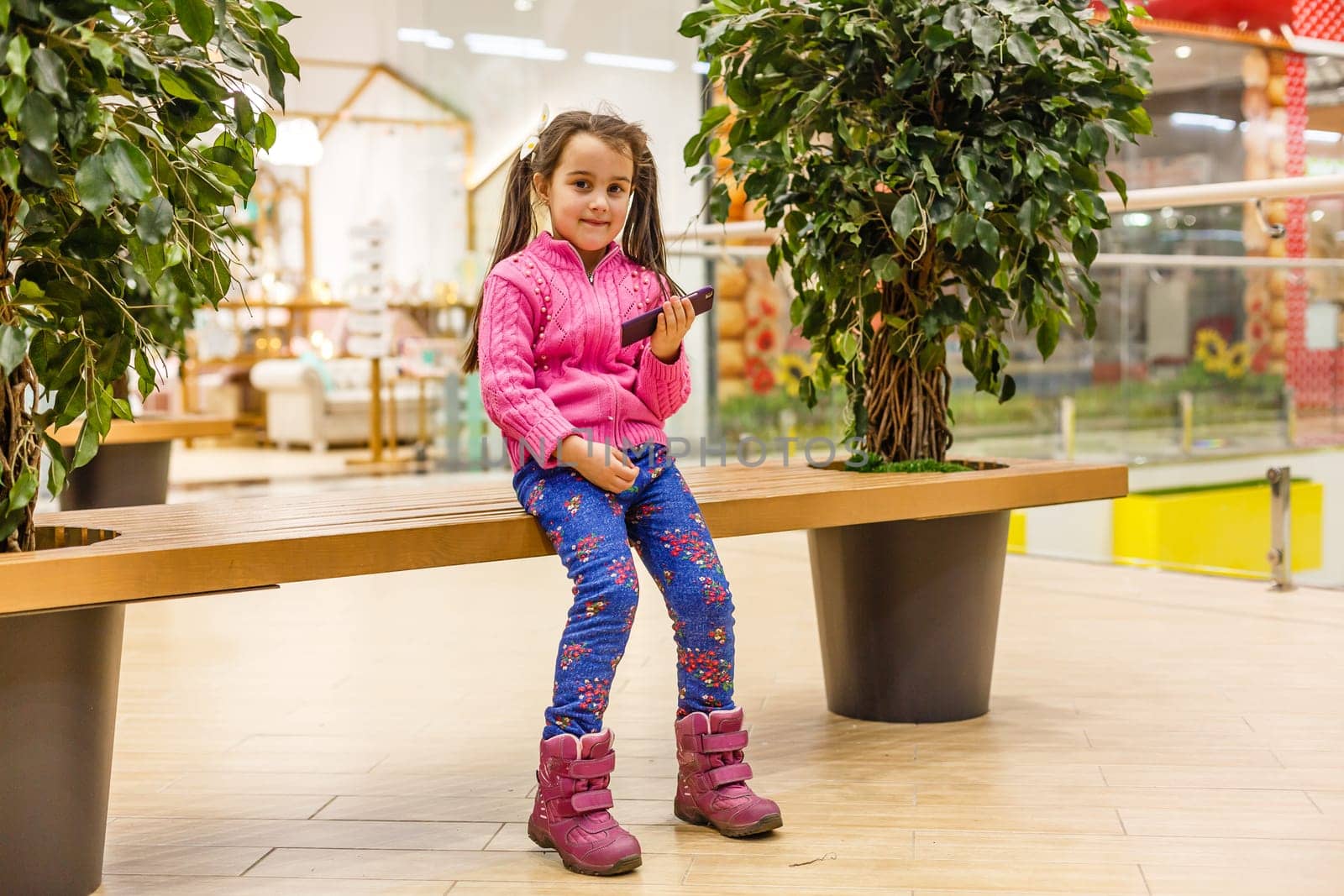 Little child girl playing with smartphone in modern commercial supermarket center. by Andelov13