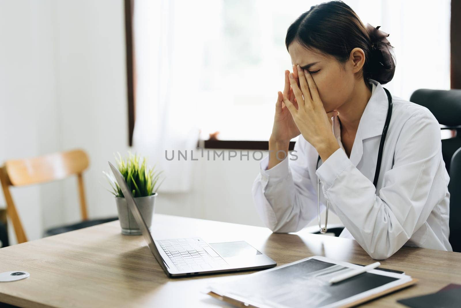 An Asian female doctor uses a computer while showing concern about patient information.