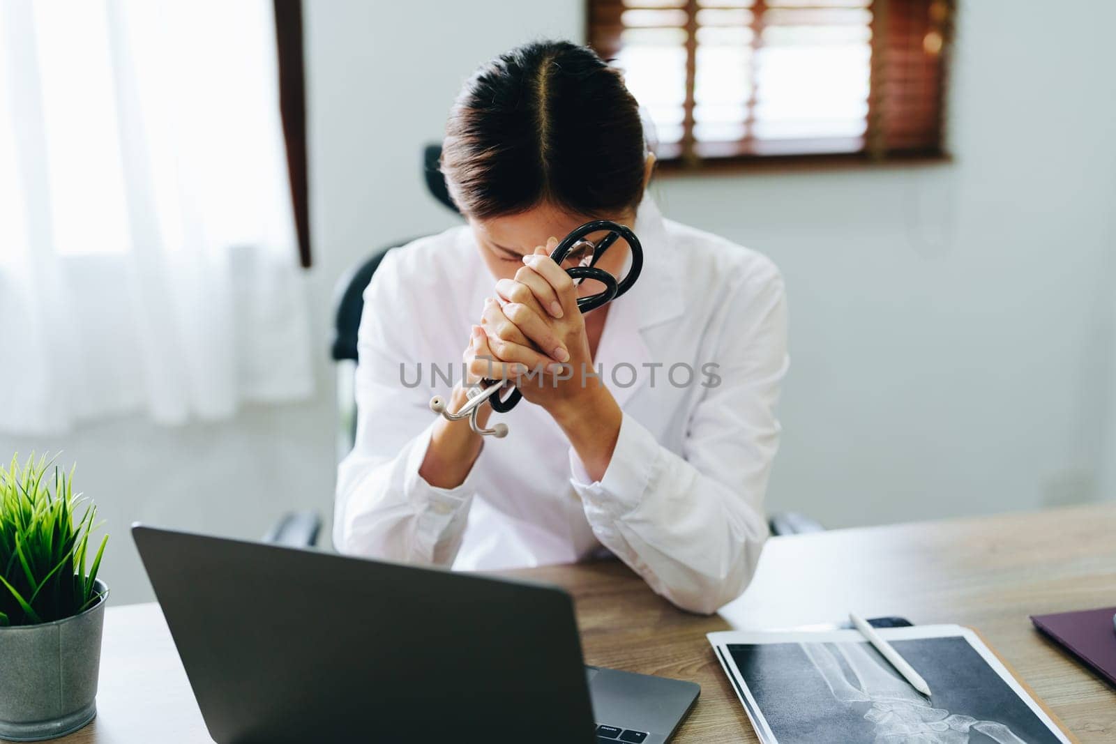 An Asian female doctor uses a computer while showing concern about patient information by Manastrong