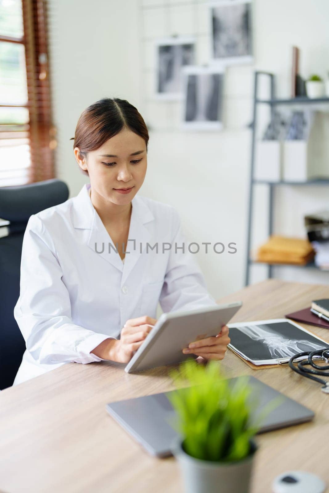 An Asian female doctor is using a tablet computer to analyze patient symptoms before treatment.