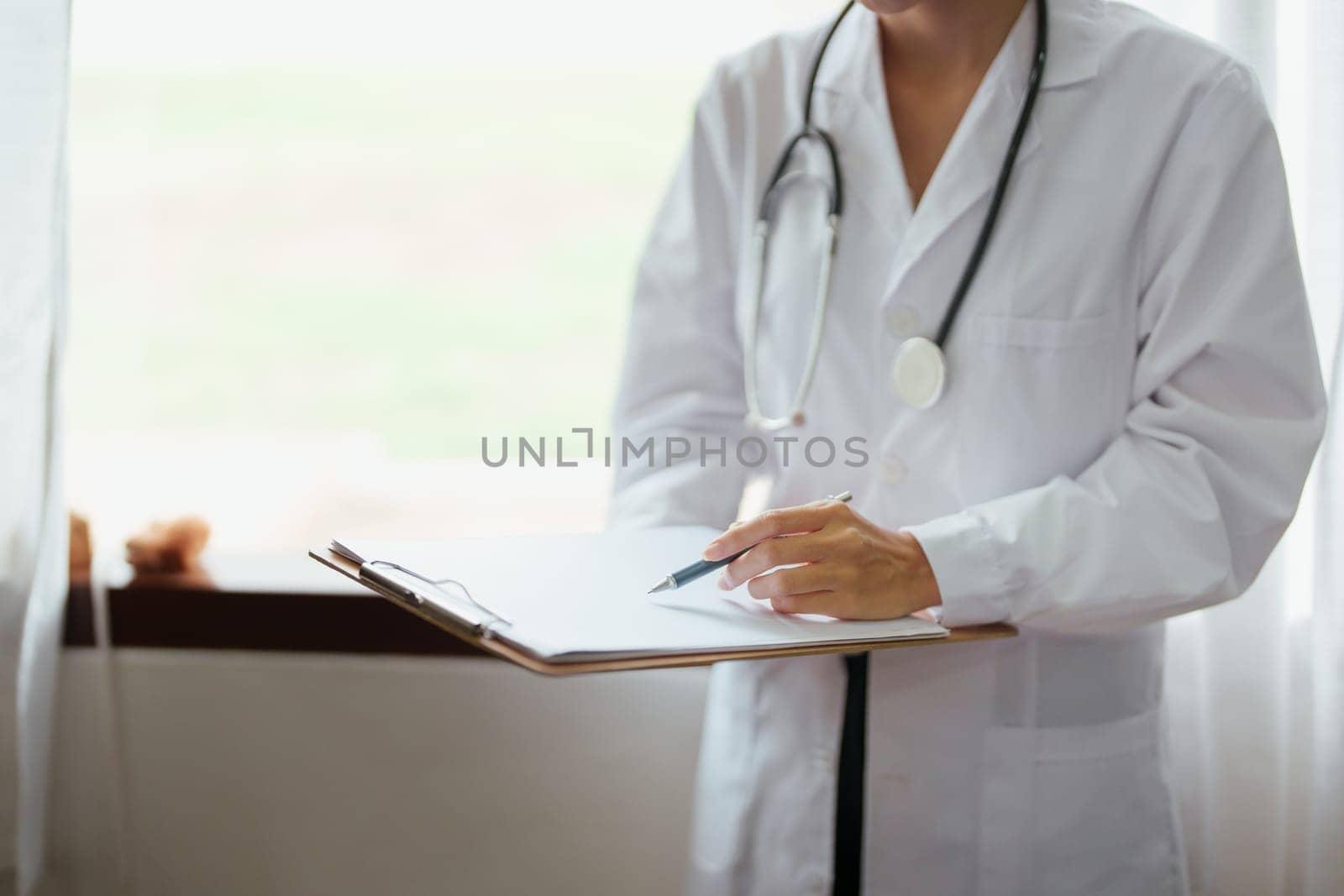 Asian female doctor holding patient information document to analyze the problem of ailments before examination by Manastrong