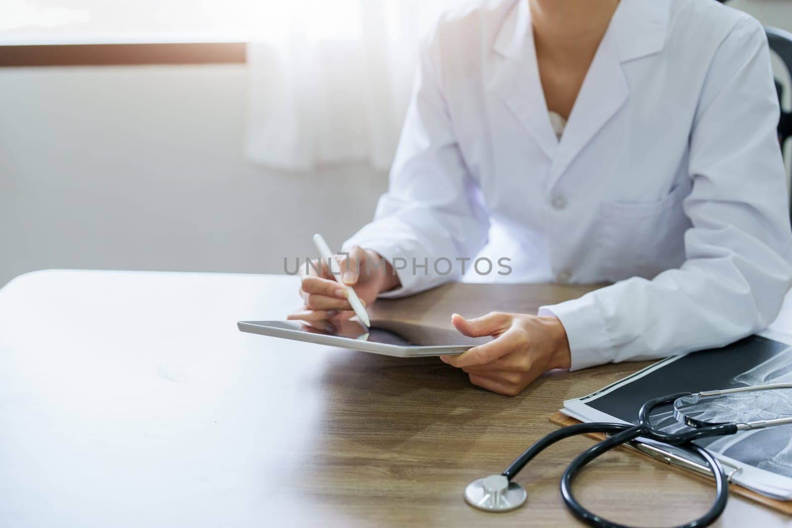 An Asian female doctor is using a tablet computer to analyze patient symptoms before treatment.