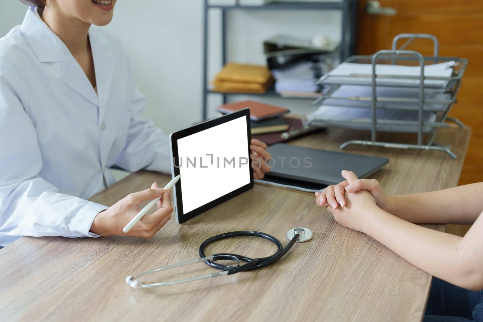 Asian female doctor holds computer tablet to customer, white screen can insert text or image by Manastrong
