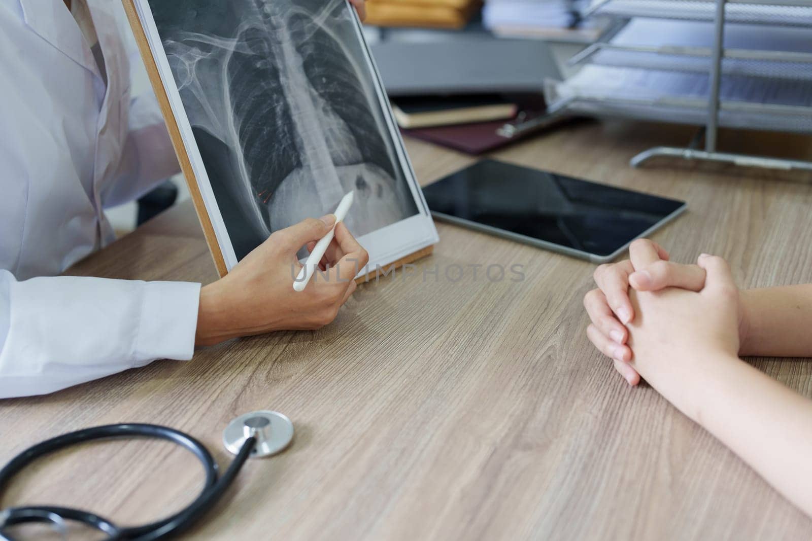 An Asian female doctor points to a patient x-ray film to explain the patient's treatment process.