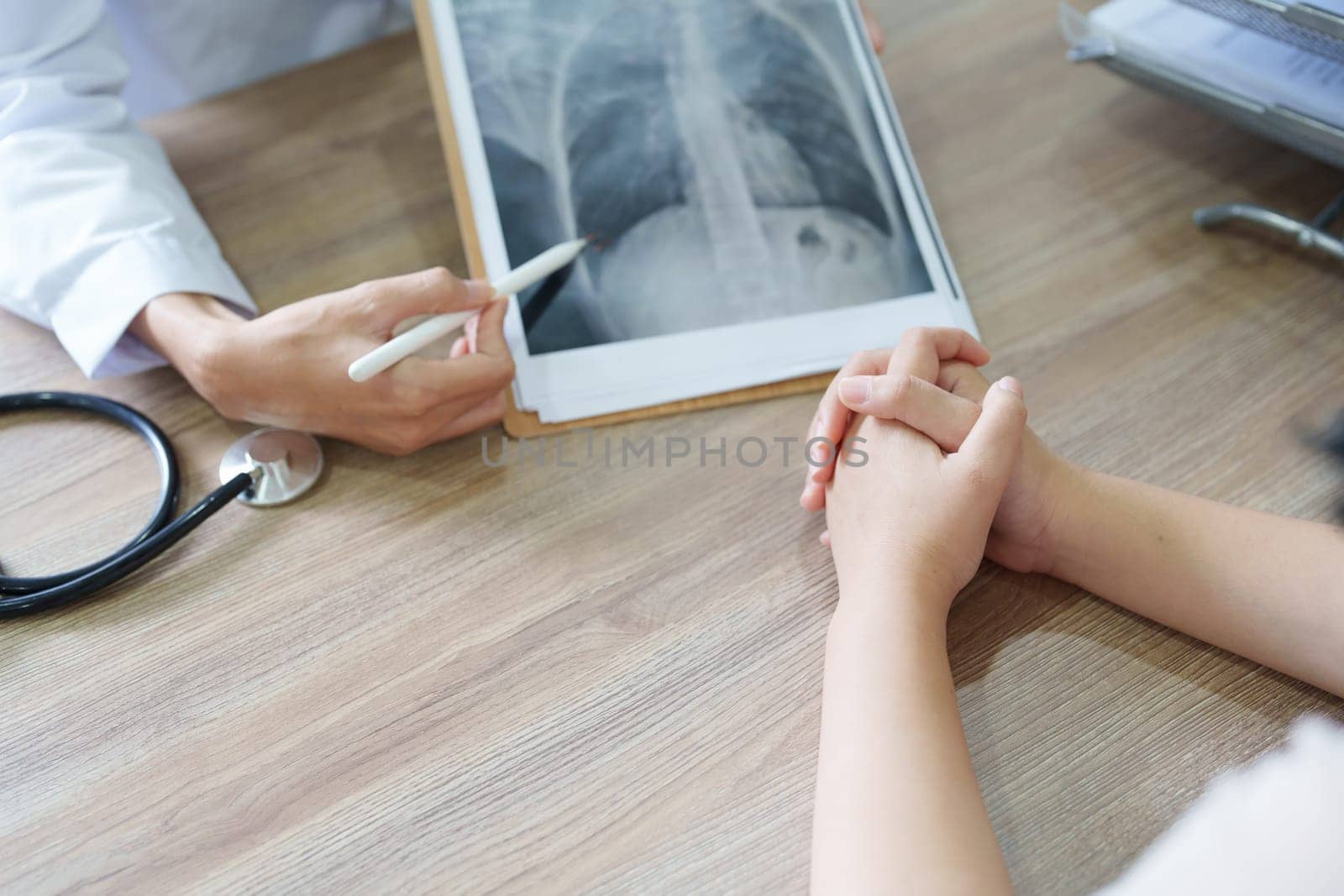 An Asian female doctor points to a patient x-ray film to explain the patient's treatment process.