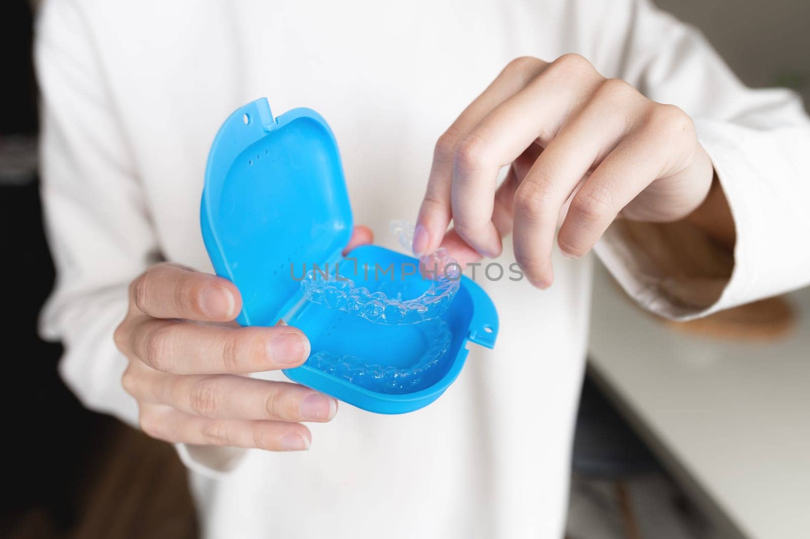 close-up of a young woman, with her hand holding a dental retainer invisible on a cream background of her jacket for the concept of a beautiful teeth treatment course.