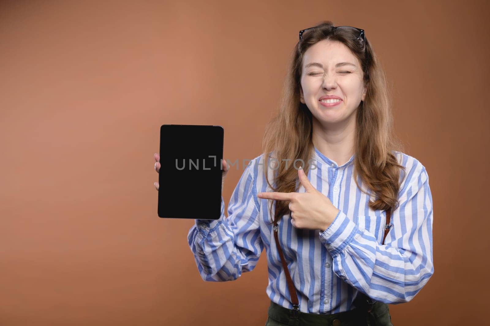Portrait of a cheerful laughing hipster woman in a shirt pointing her finger at the screen of a tablet computer. Modern youth.