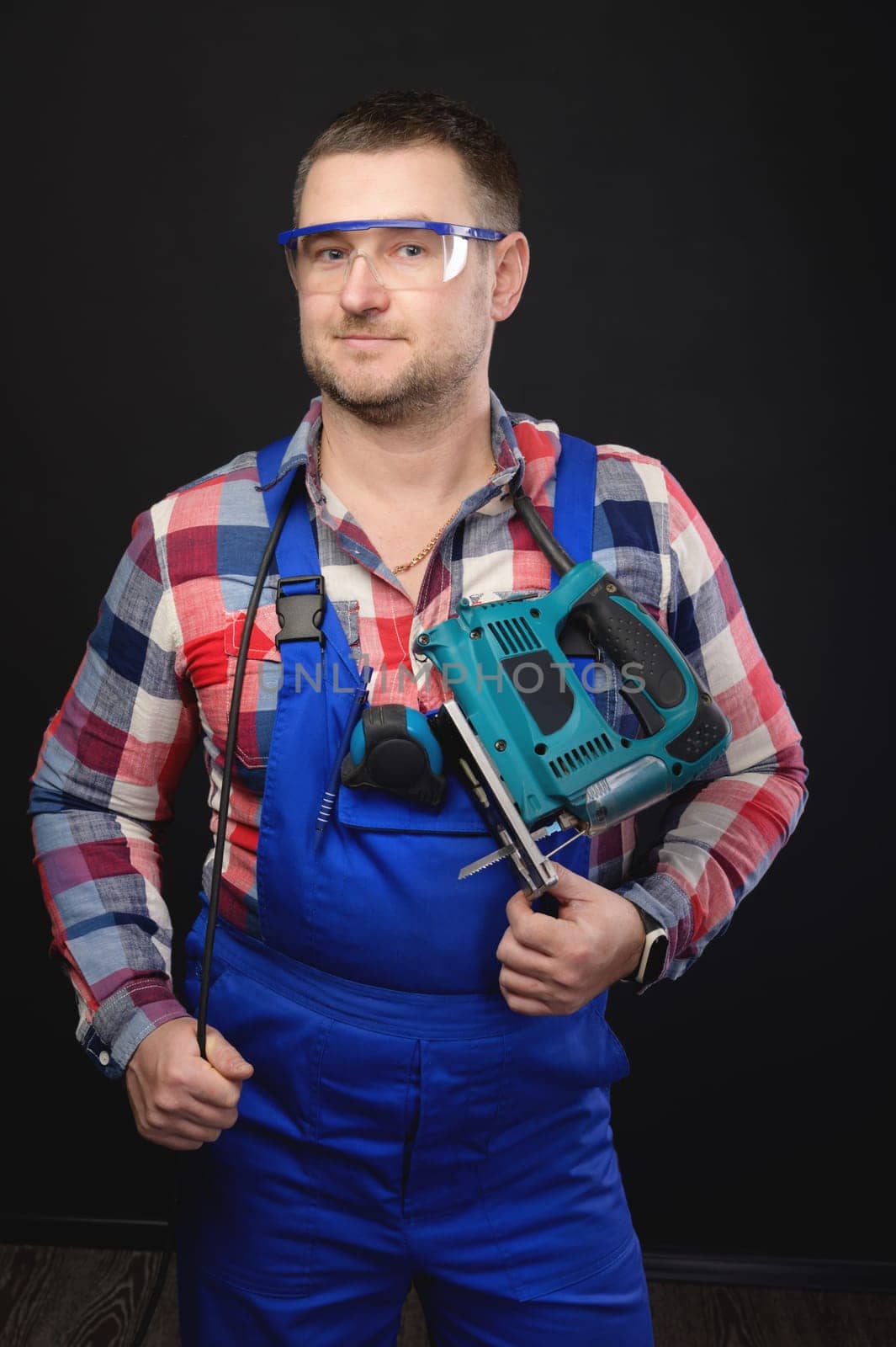 Handsome smiling man, carpenter stands with electric jigsaw, portrait. Making furniture to order.