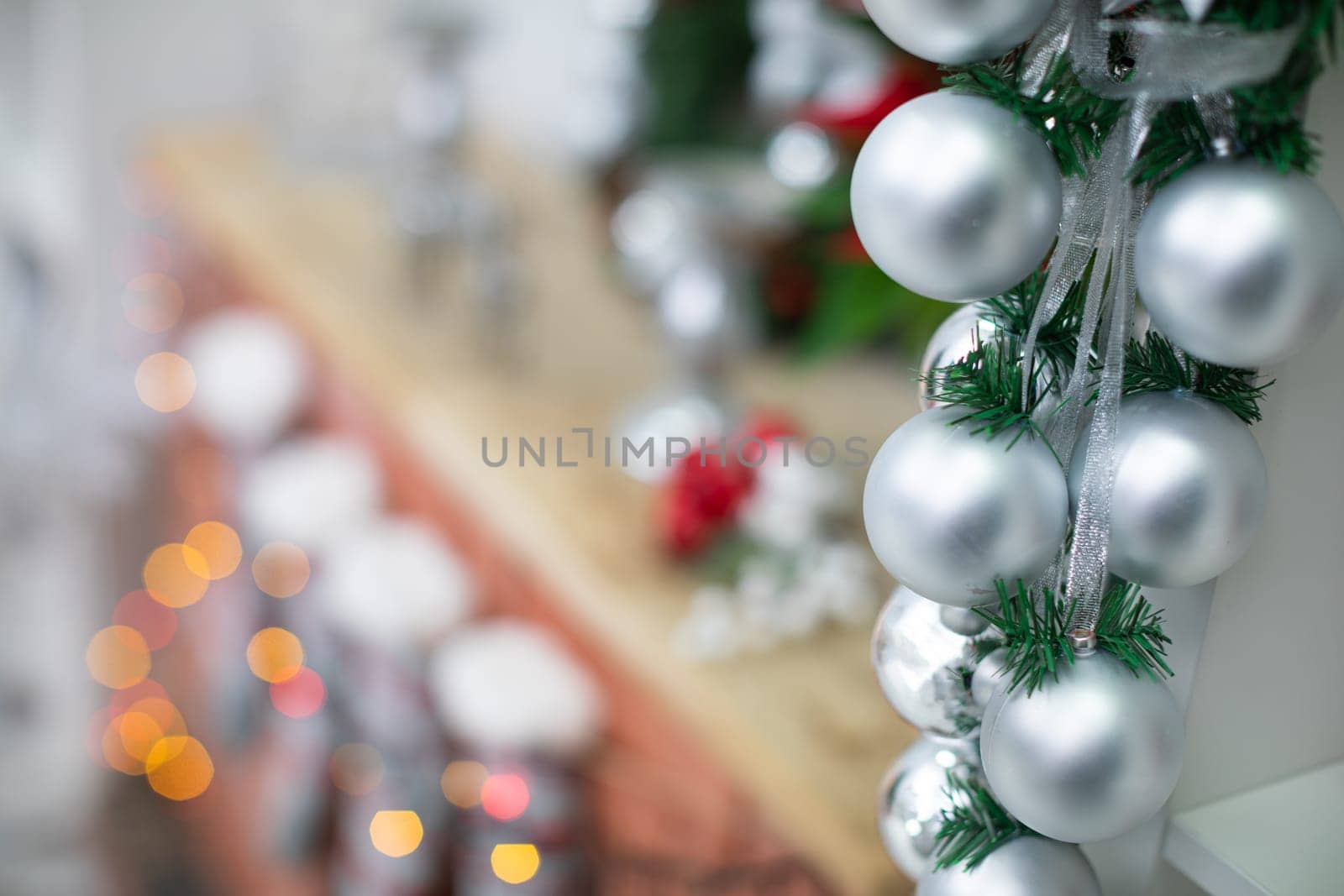 Silver baubles on spruce twigs and decorated fireplace in background.