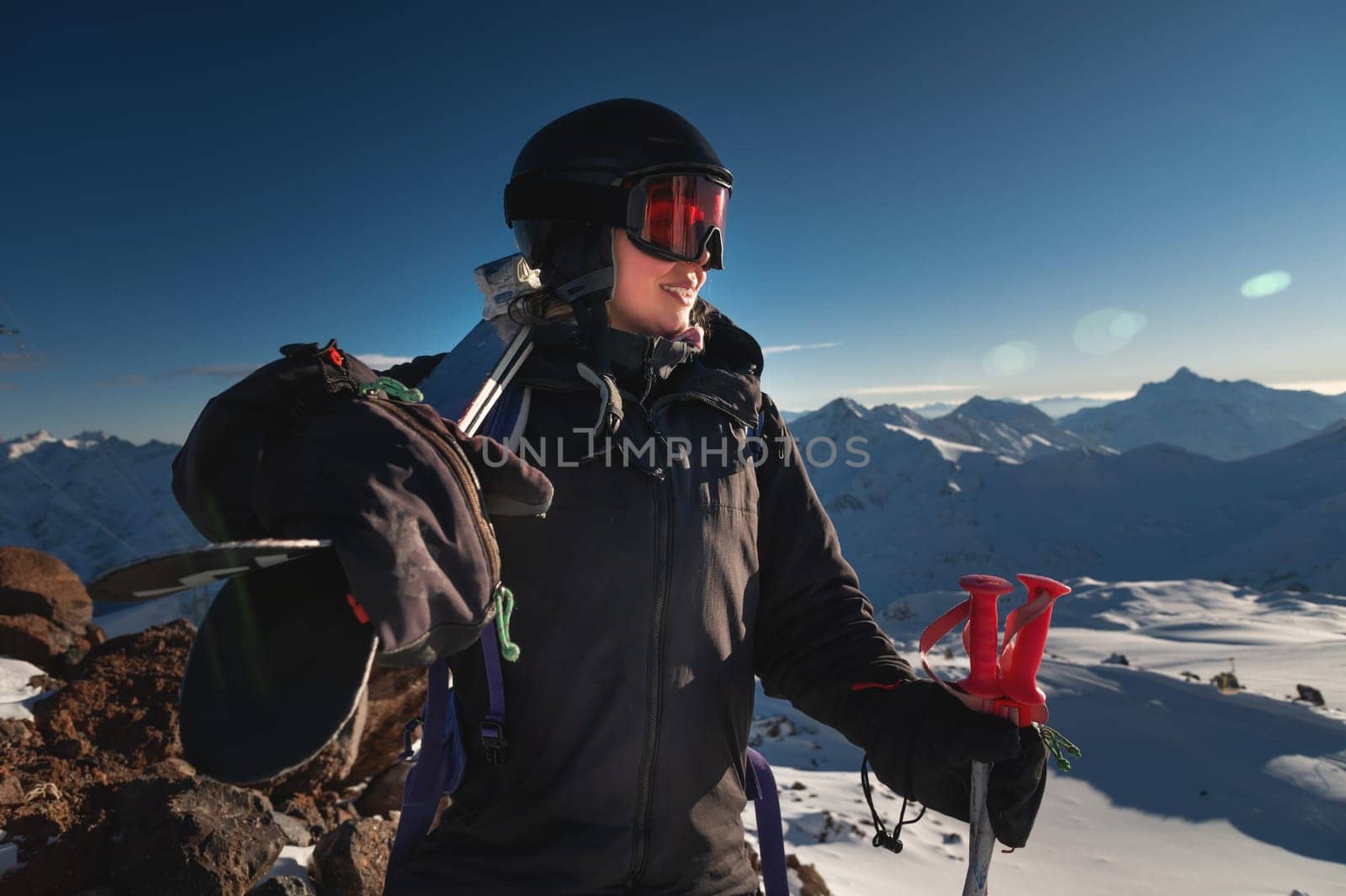 Image of a woman with skis on her shoulder against a snowy hill or mountain range. Portrait of a cheerful skier carrying skis on her shoulder by yanik88