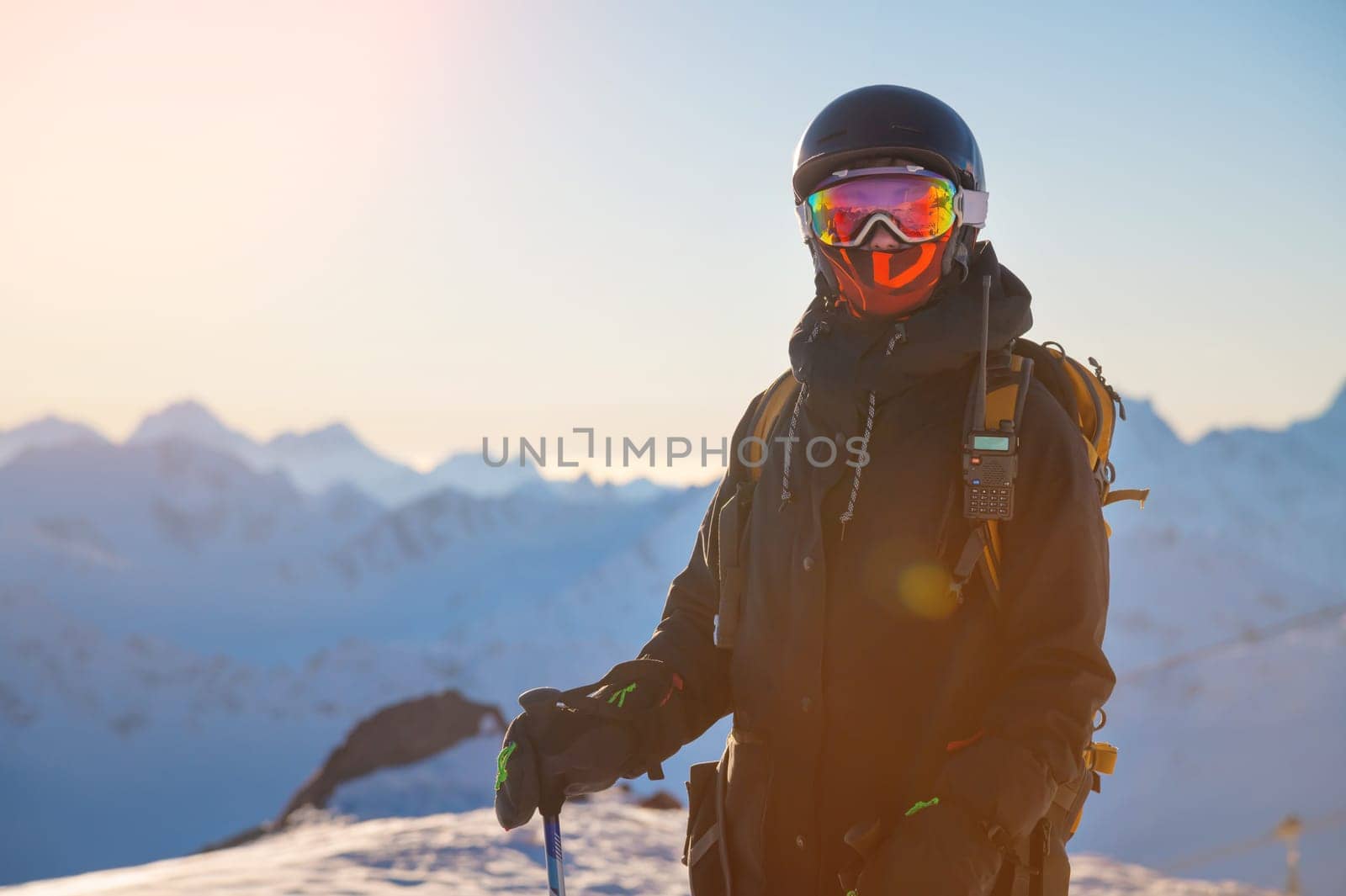 Portrait of a skier on the mountain at sunset. Portrait of a woman in a ski resort against the backdrop of mountains and blue sky. Winter sports, security, protection and radio communication by yanik88
