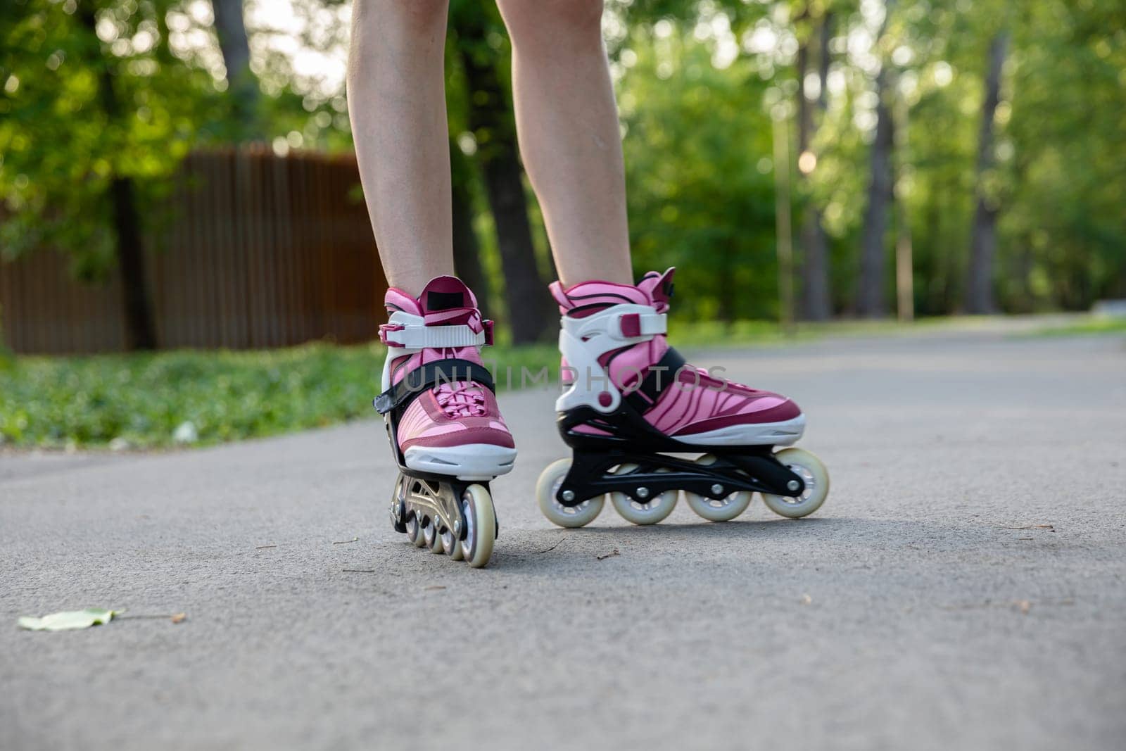 Skater girl riding rollerblades in the park. Rollerblades in fashionable purple and gray colors. Well-fitting sports equipment. Playing sports outdoors.