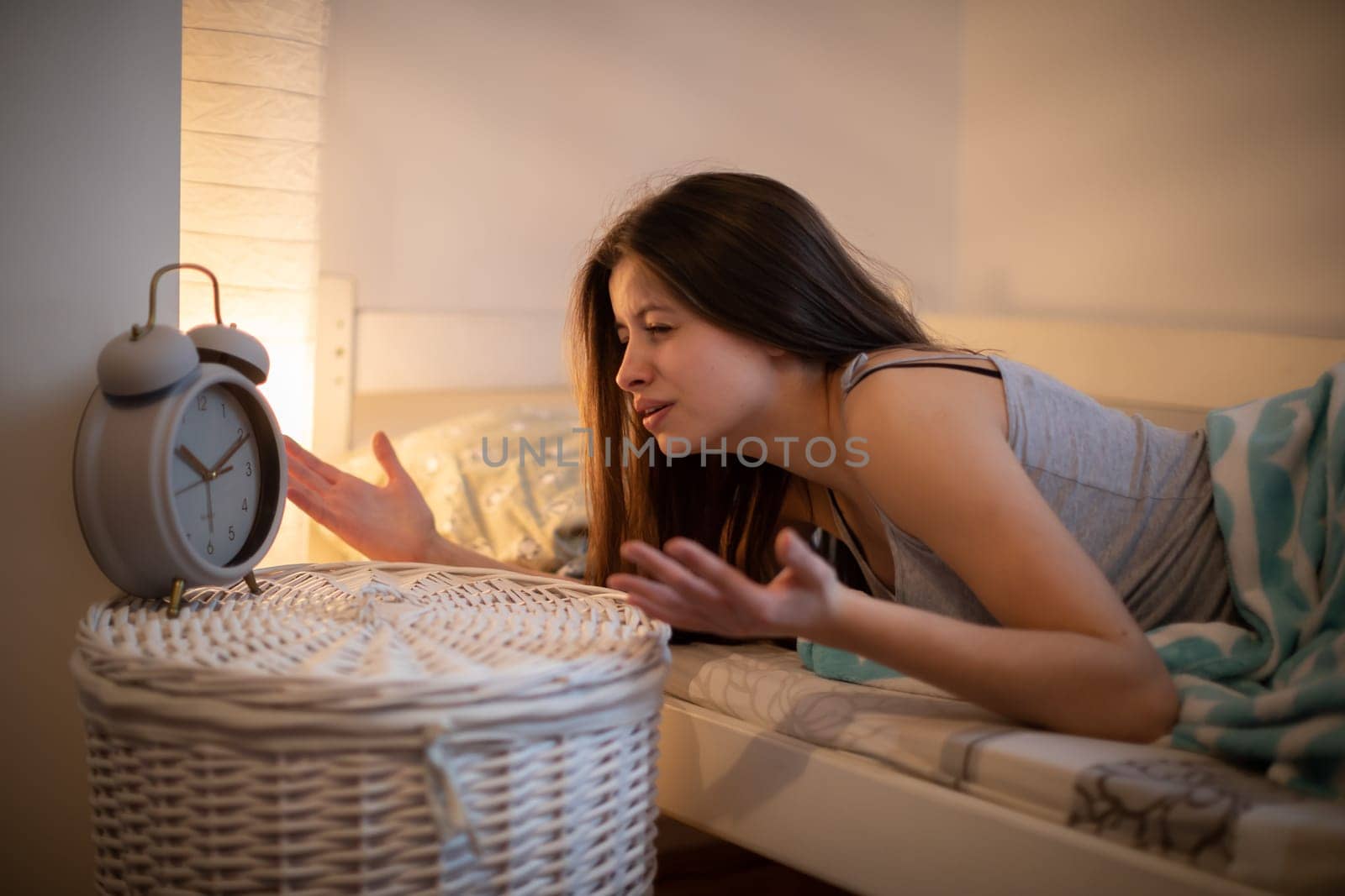 Bedroom in bright colors. The annoyed woman looks at her bedside watch.