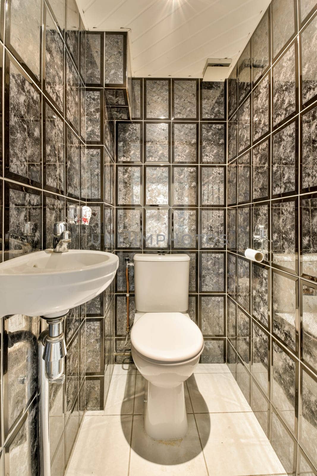 a bathroom with black and white tiles on the walls, along with a toilet in front of a mirror wall