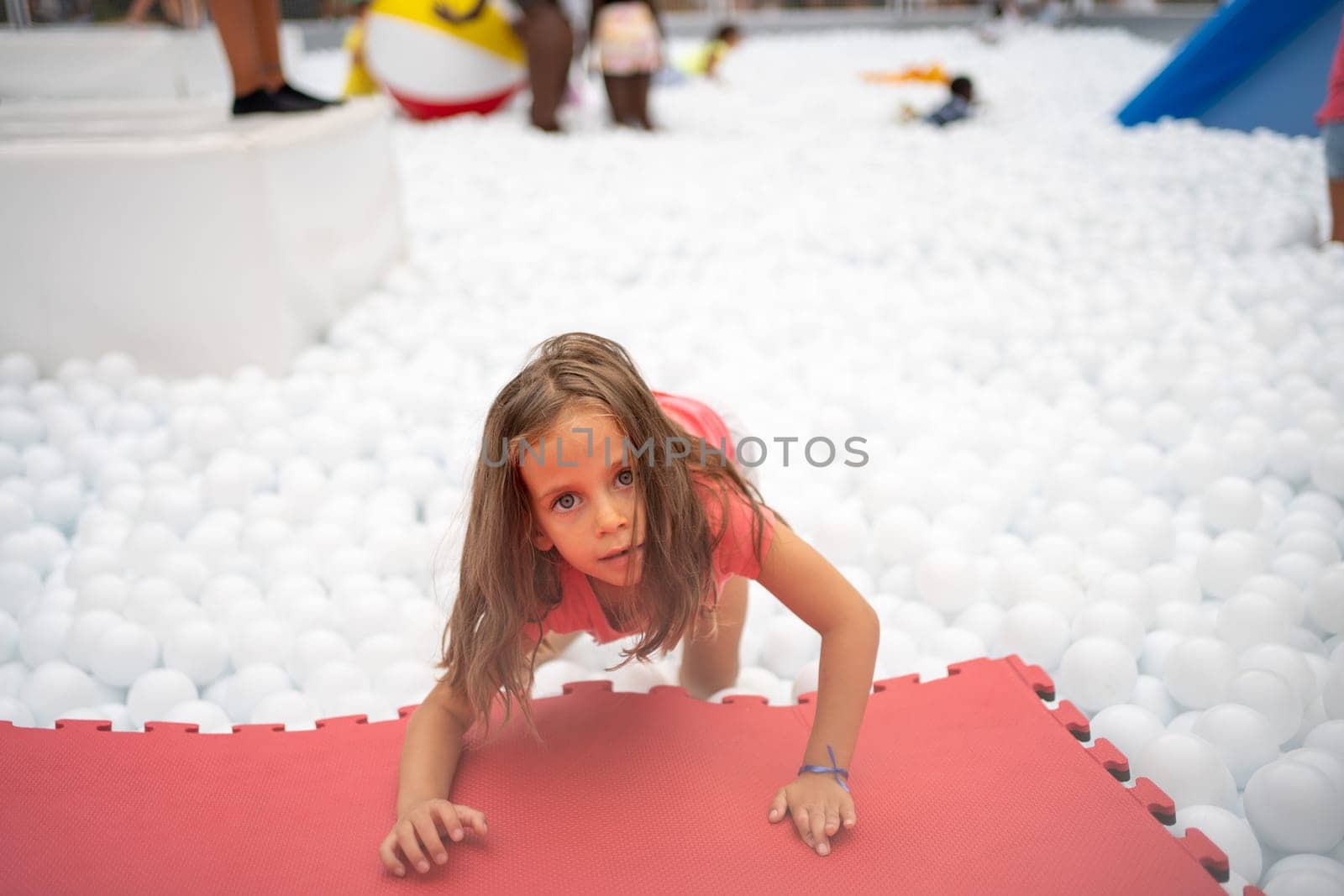 Happy little girl playing white plastic balls pool in amusement park. playground for kids. Active leisure for children.