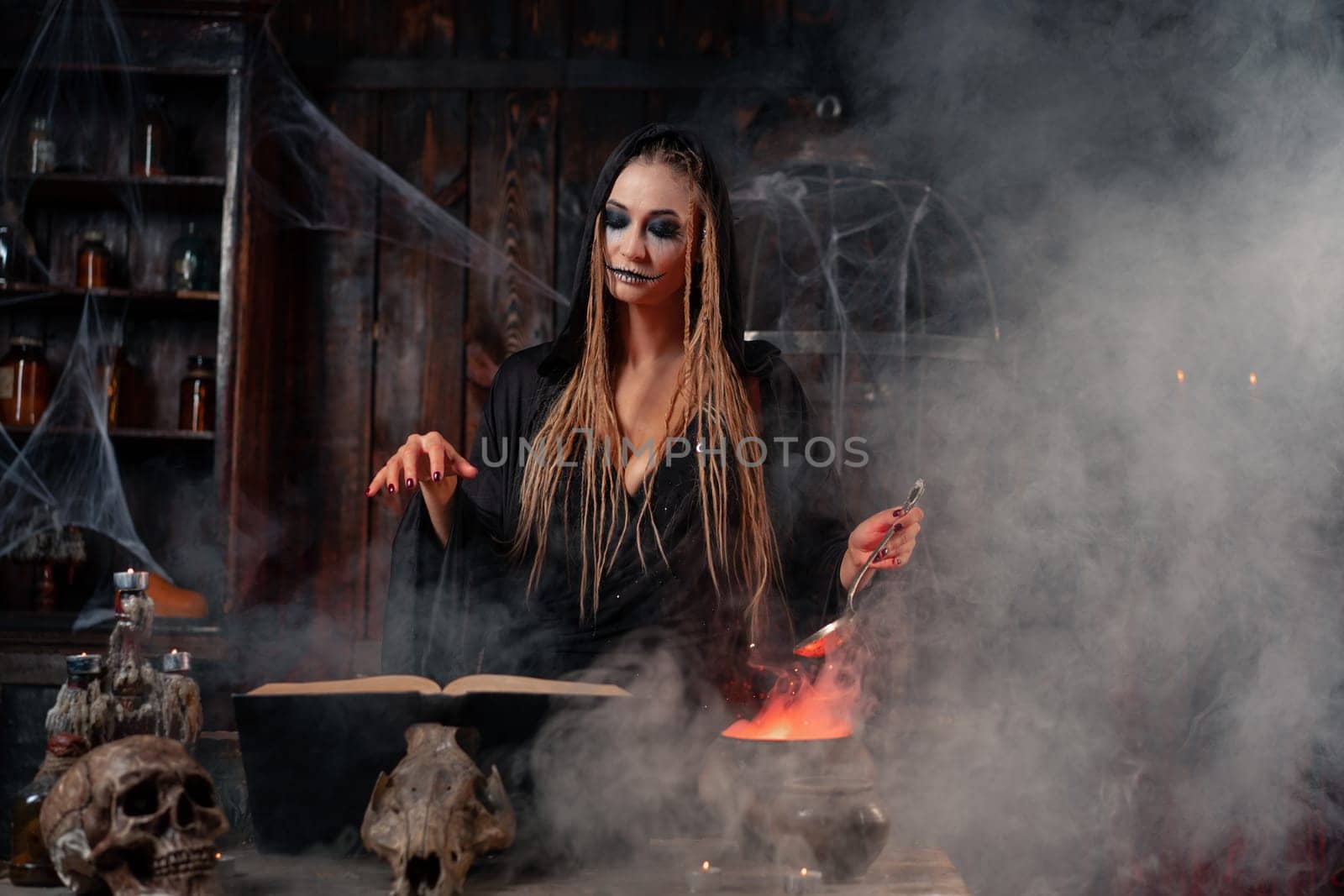 Halloween, witch use magic book and cauldron prepare poison or love potion. Black magic occult female wizard in dark room cage spider web human skull. Necromancer cooking magic potion. Smoke