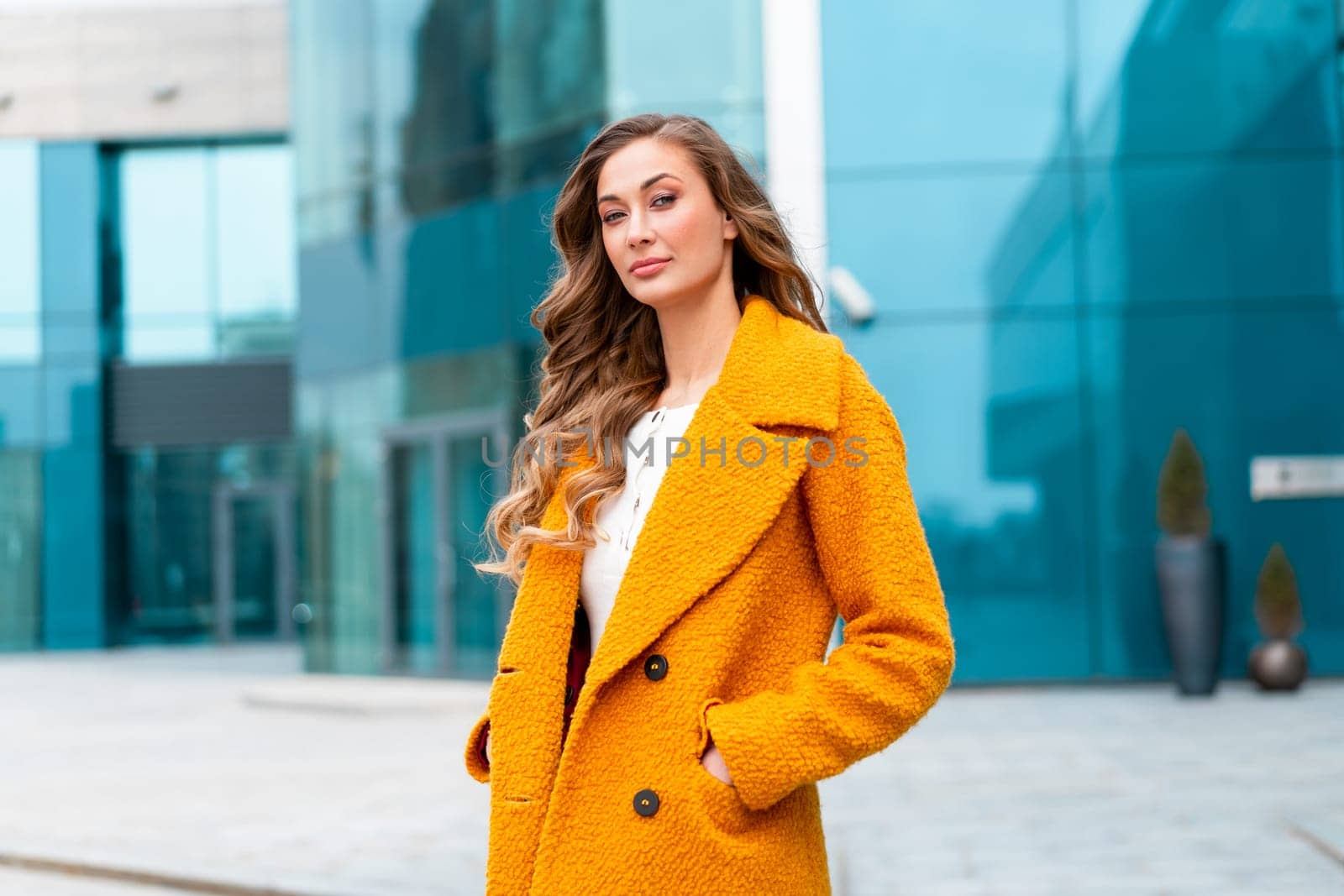 Business woman dressed yellow coat standing outdoors corporative building background Caucasian female business person on city street near office building with windows Stylish businesswoman