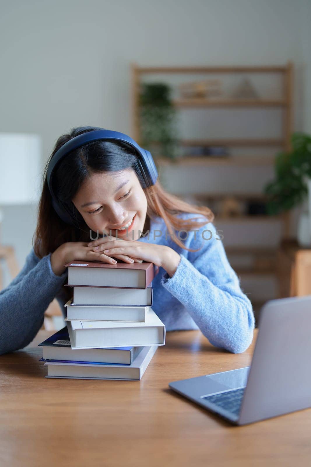 Portrait of young beautiful Asian woman showing smiling face during early morning online class with books, headphones and computer as study materials at home by Manastrong