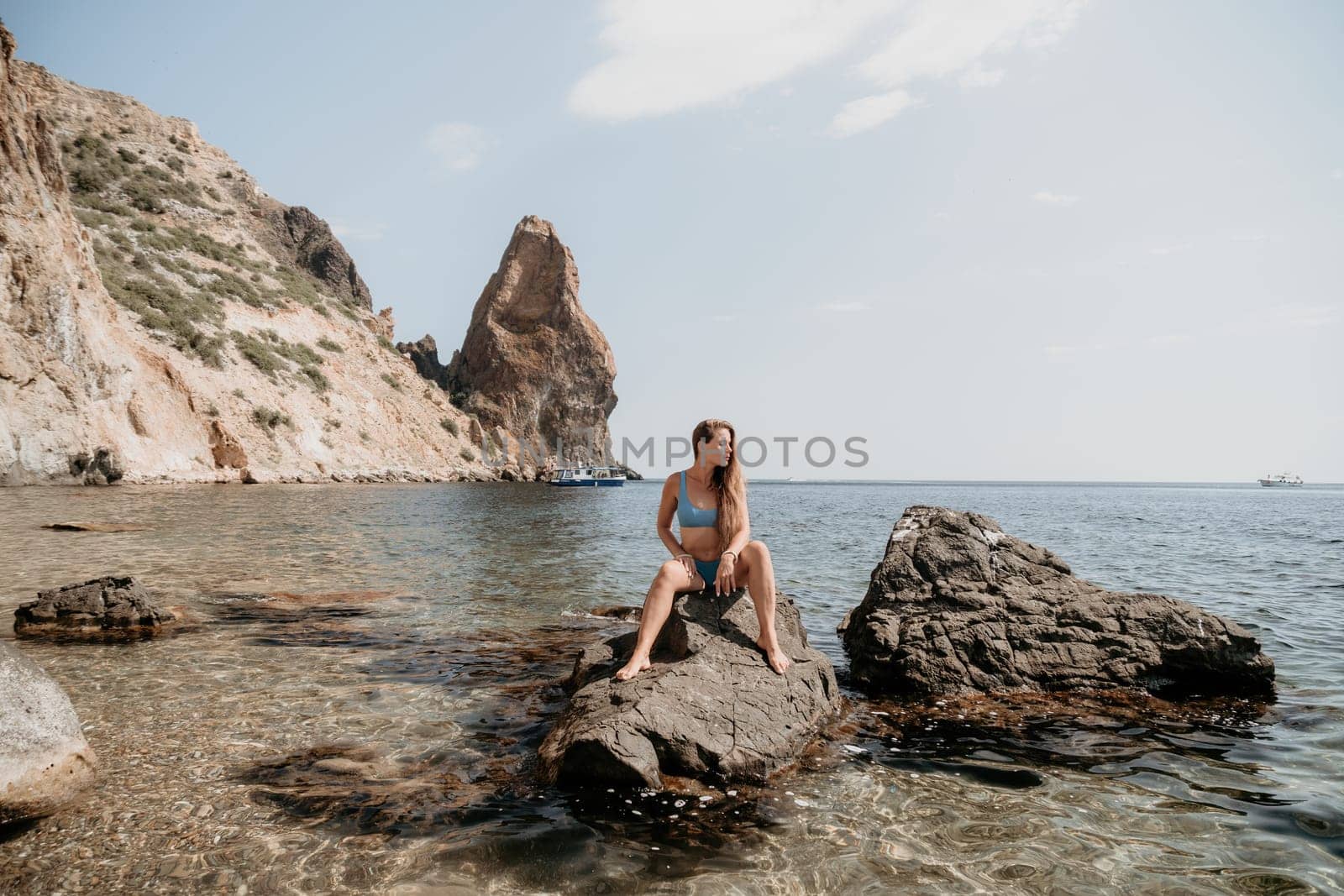 Woman travel sea. Young Happy woman in a long red dress posing on a beach near the sea on background of volcanic rocks, like in Iceland, sharing travel adventure journey