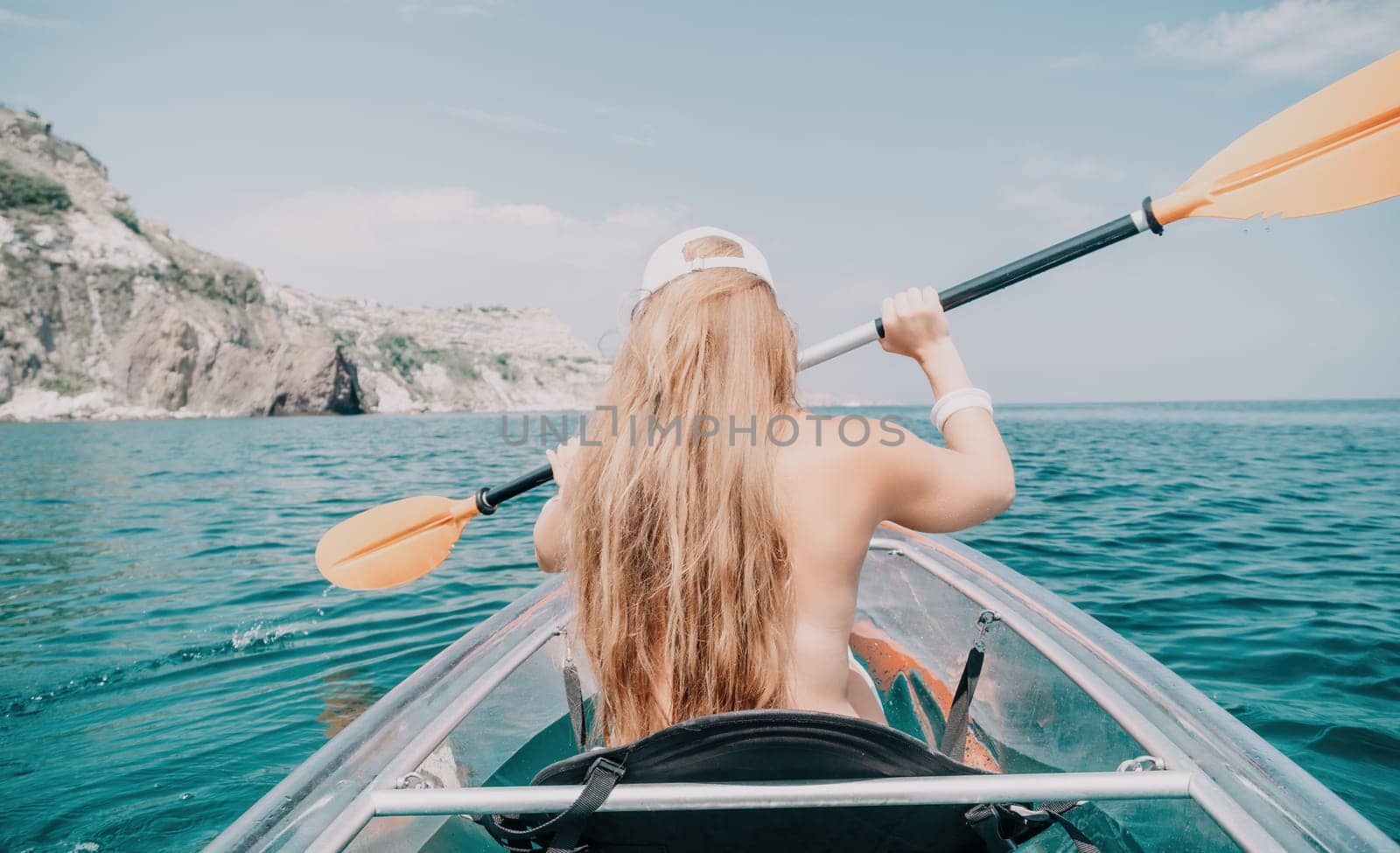 Woman in kayak back view. Happy young woman with long hair floating in transparent kayak on the crystal clear sea. Summer holiday vacation and cheerful female people having fun on the boat.