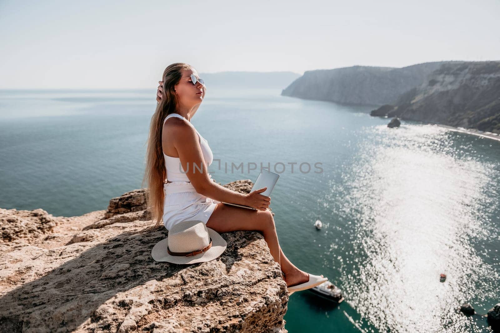 Digital nomad, Business woman working on laptop by the sea. Pretty lady typing on computer by the sea at sunset, makes a business transaction online from a distance. Freelance, remote work on vacation by panophotograph