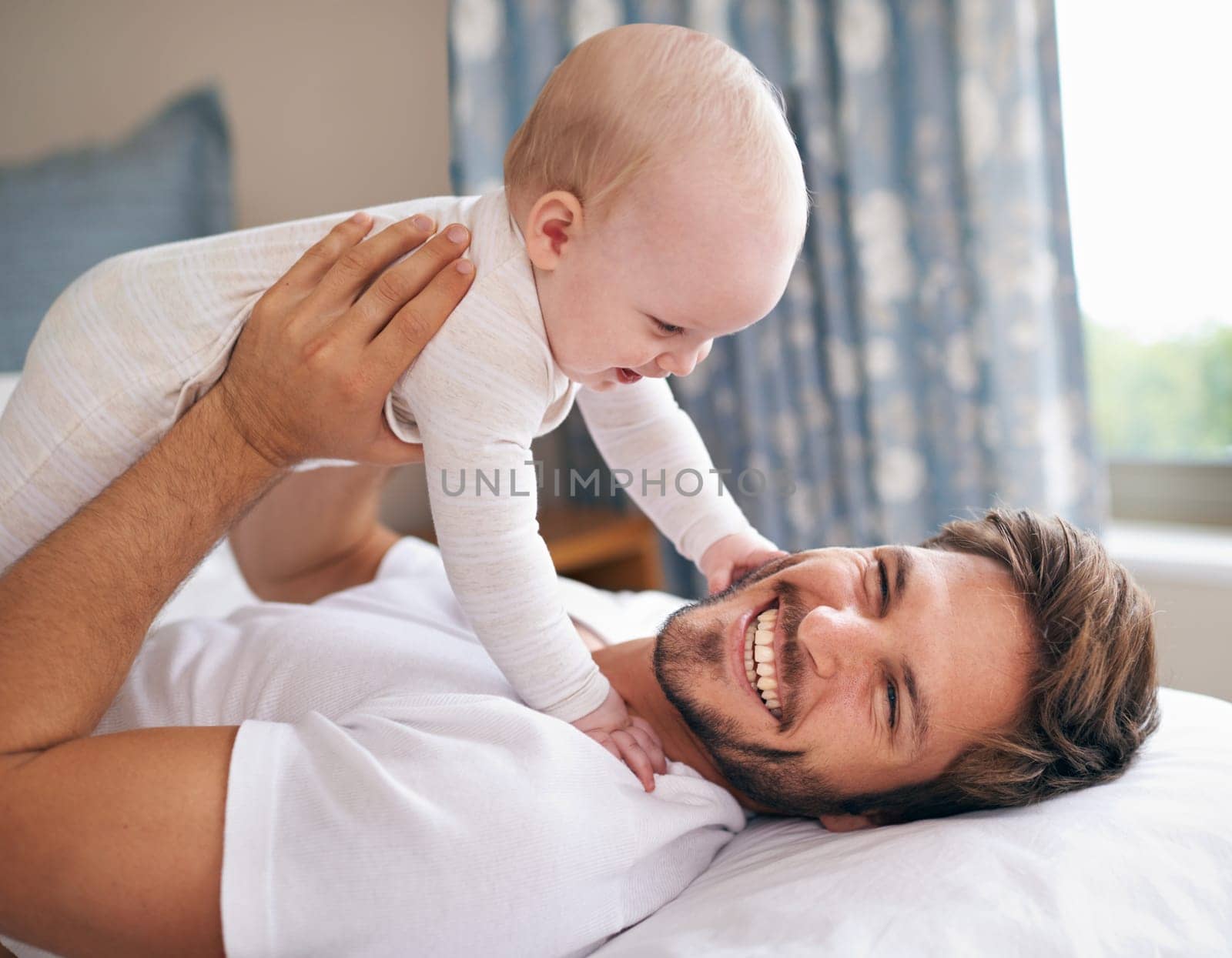 I love grabbing daddys beard. a father lying on a bed holding his baby girl up in the air