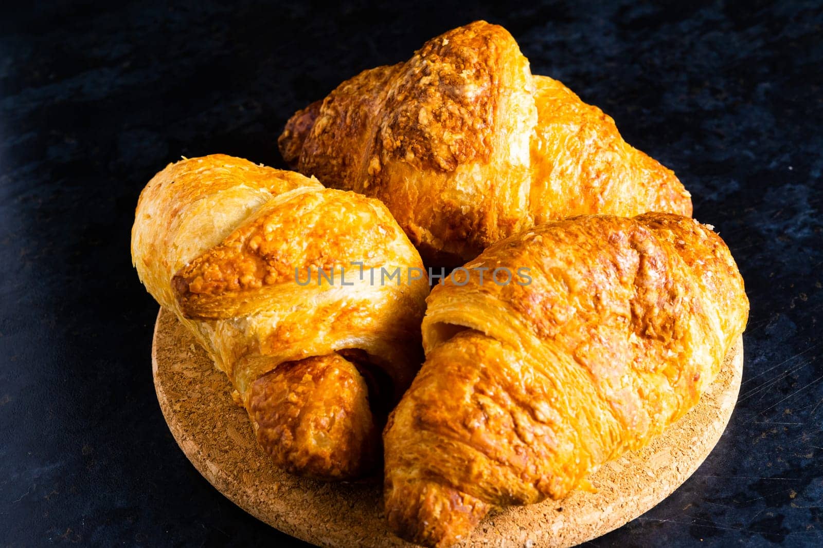 Freshly backed french croissant shiny in the rays of morning sun, dark background, kitchen