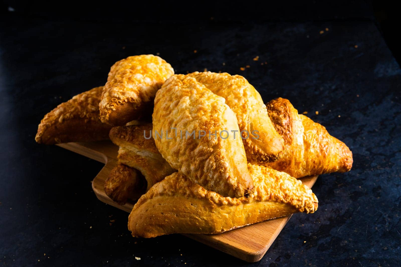 Freshly backed french croissant shiny in the rays of the morning sun, dark background, kitchen by Zelenin