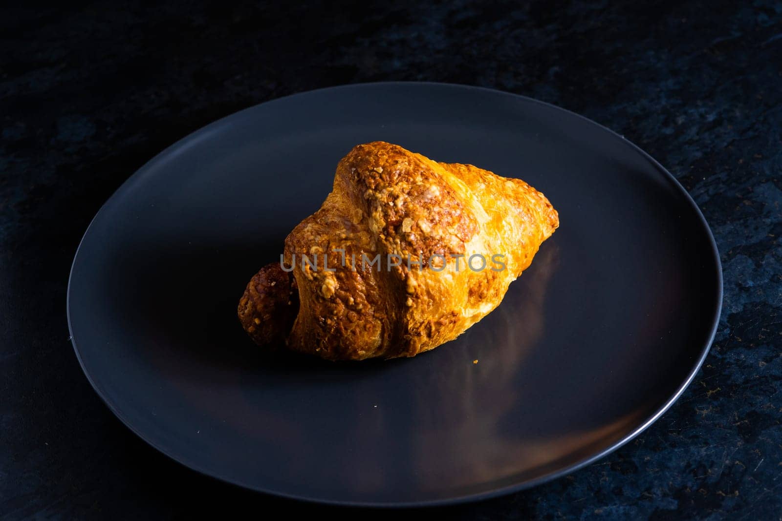 Freshly backed french croissant shiny in the rays of the morning sun, dark background, kitchen by Zelenin