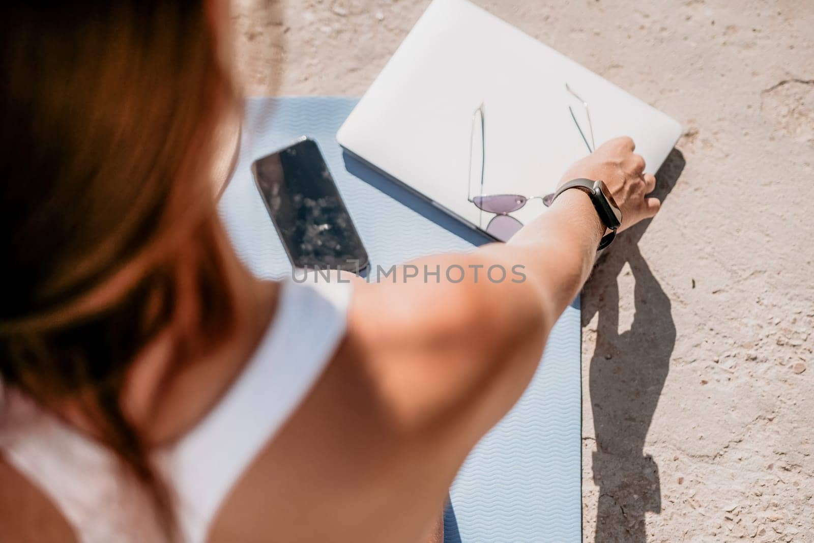 Successful business woman in yellow hat working on laptop by the sea. Pretty lady typing on computer at summer day outdoors. Freelance, travel and holidays concept.