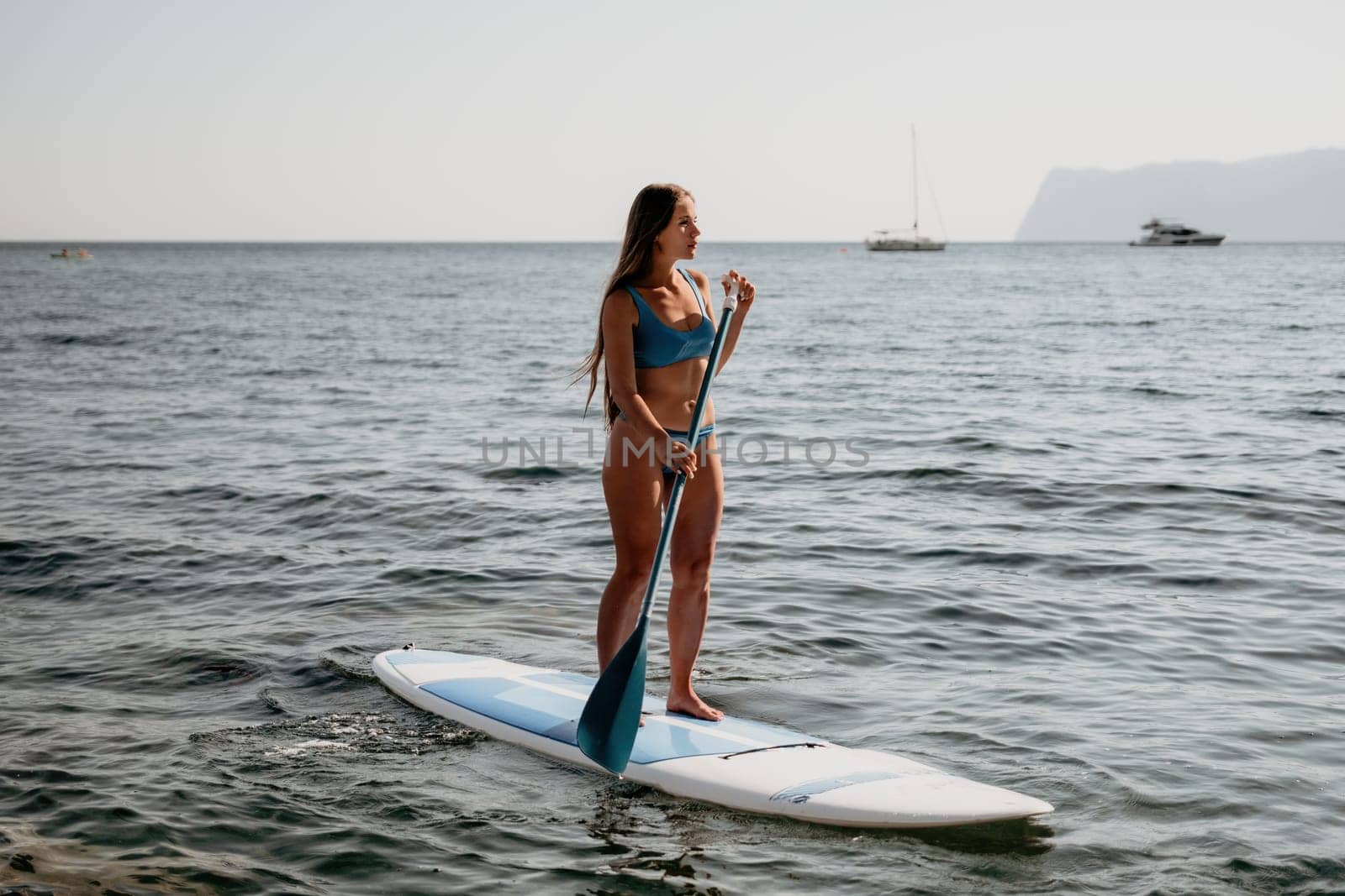 Close up shot of happy young caucasian woman looking at camera and smiling. Cute woman portrait in bikini posing on a volcanic rock high above the sea