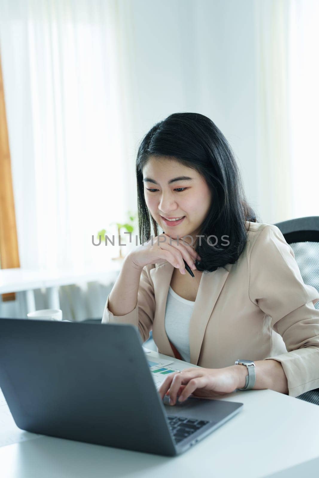 Portrait of a thoughtful Asian businesswoman looking at financial statements and making marketing plans using a computer on her desk.