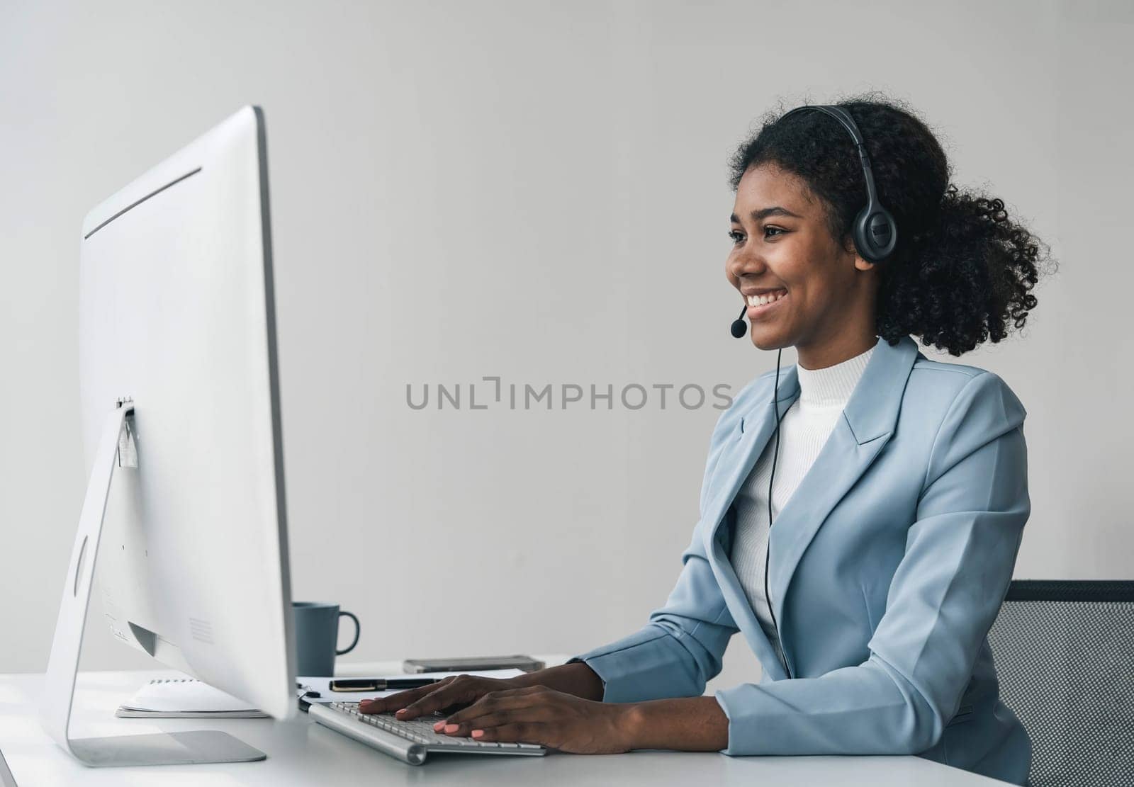 close up call center operator in wireless headset talking with customer, woman in headphones with microphone consulting client on phone in customer support service, looking at computer screen by wichayada