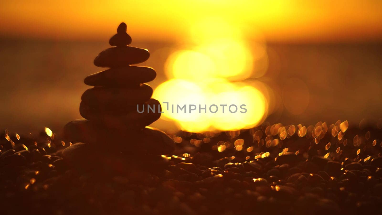 Balanced rock pyramid on pebbles beach. Golden sea bokeh on background. Selective focus, zen stones on sea beach, meditation, spa, harmony, calm, balance concept