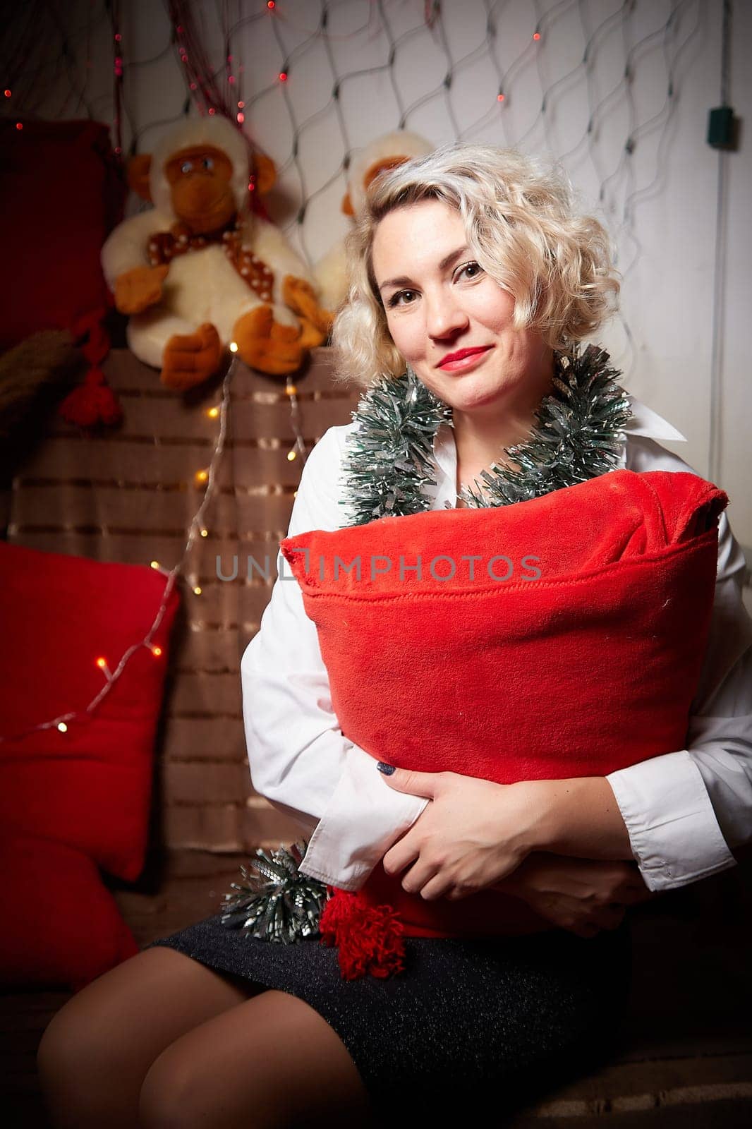 An elegant blonde girl in a white blouse in a room decorated for Christmas or new year with a background, tinsel and light garlands by keleny