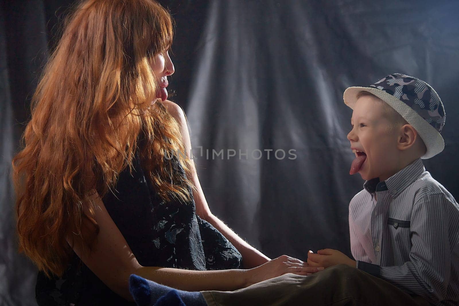 Woman with boy in hat. Mom with son on a dark background. Family portrait with mother with red hair and boy having fun together