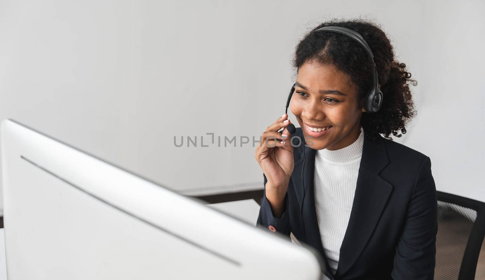 close up call center operator in wireless headset talking with customer, woman in headphones with microphone consulting client on phone in customer support service, looking at computer screen by wichayada