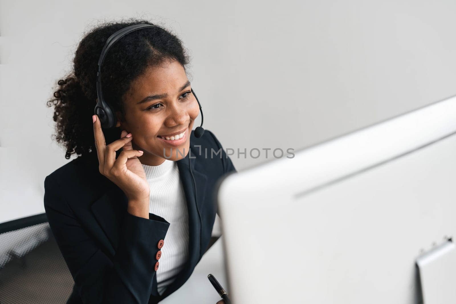 close up call center operator in wireless headset talking with customer, woman in headphones with microphone consulting client on phone in customer support service, looking at computer screen by wichayada